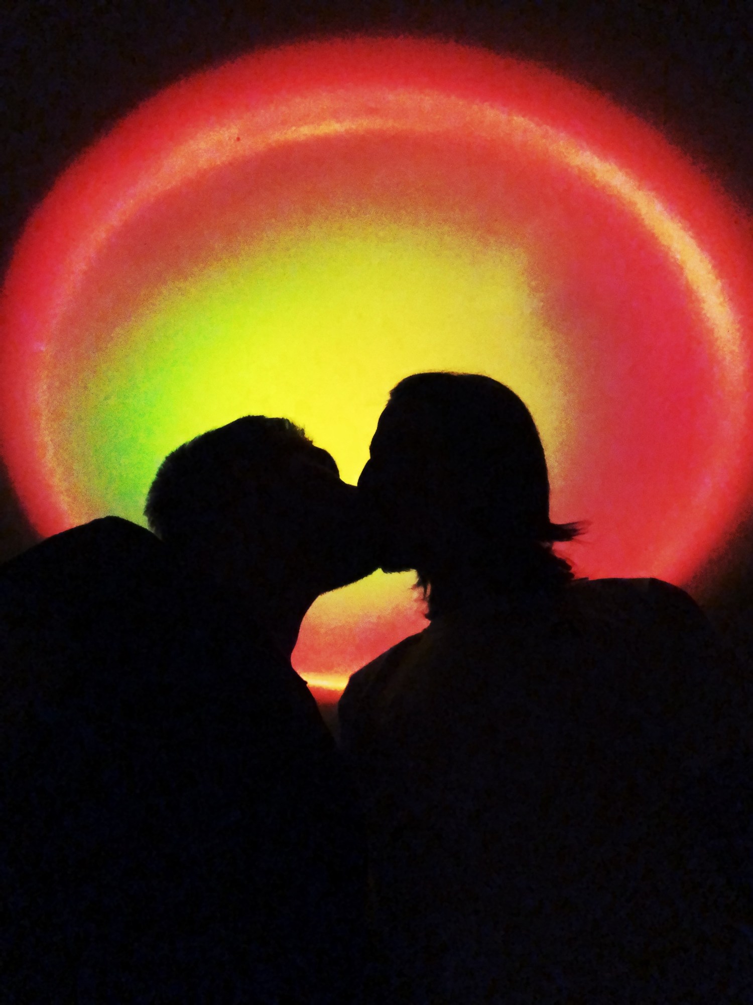 The silhouette of a couple kissing in front of a blazing red and yellow light.