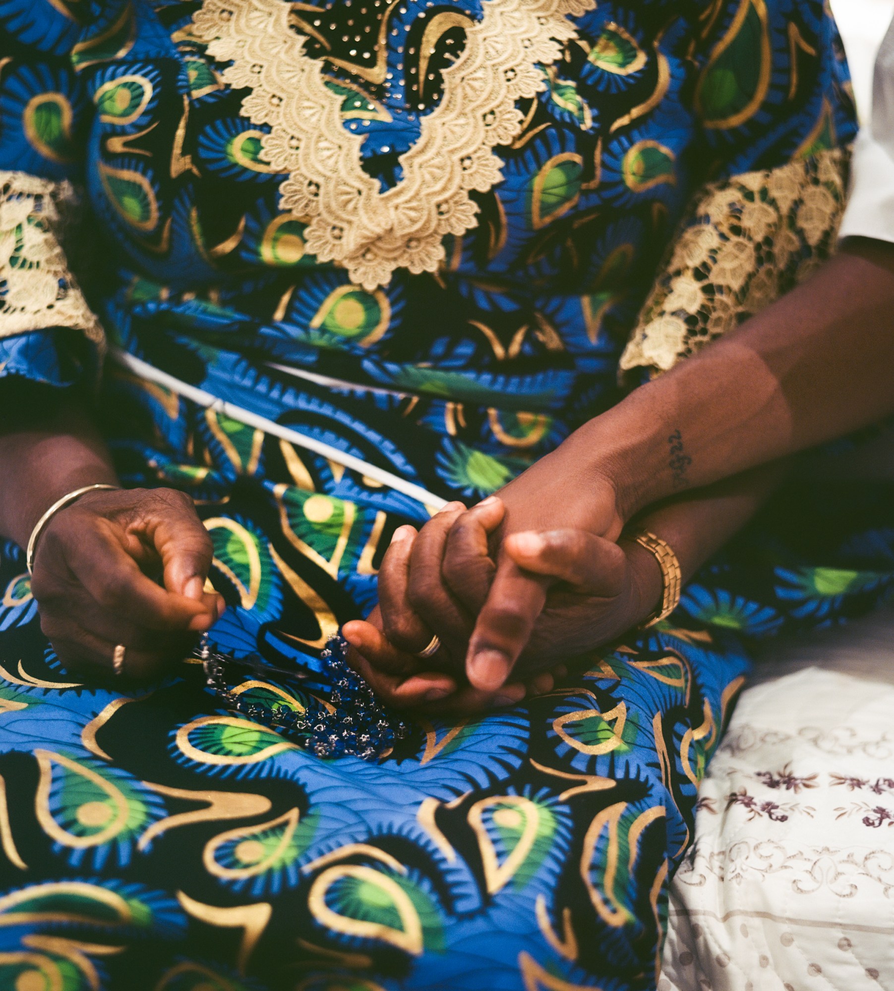 A woman in a traditional colourful printed dress holds the hand of someone else with a number tattoo.