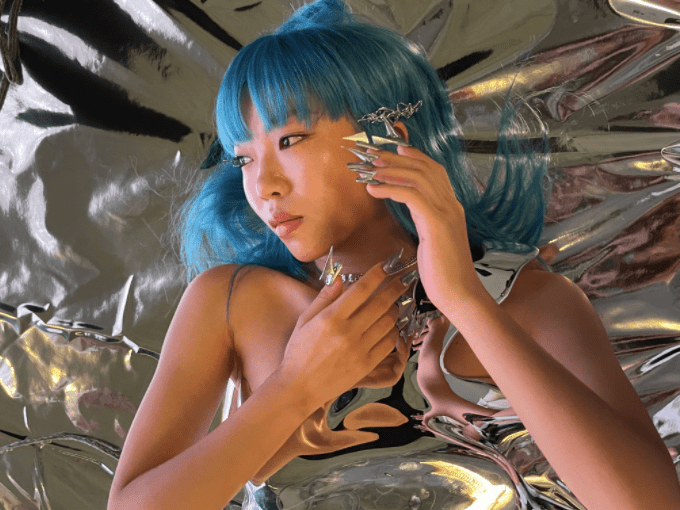 a girl with blue hair wearing long silver nails and surreal jewellery