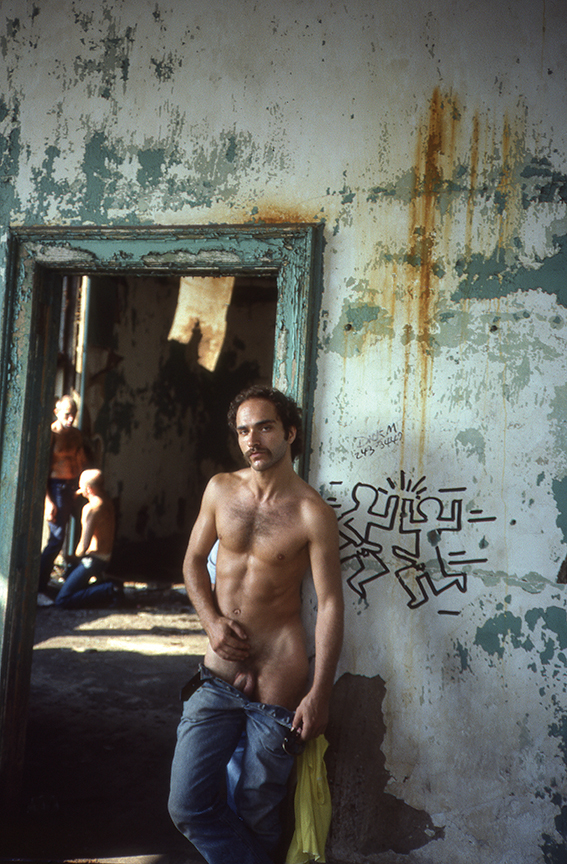 a naked man standing with his pants pulled down against a wall at christopher street pier in the 70s