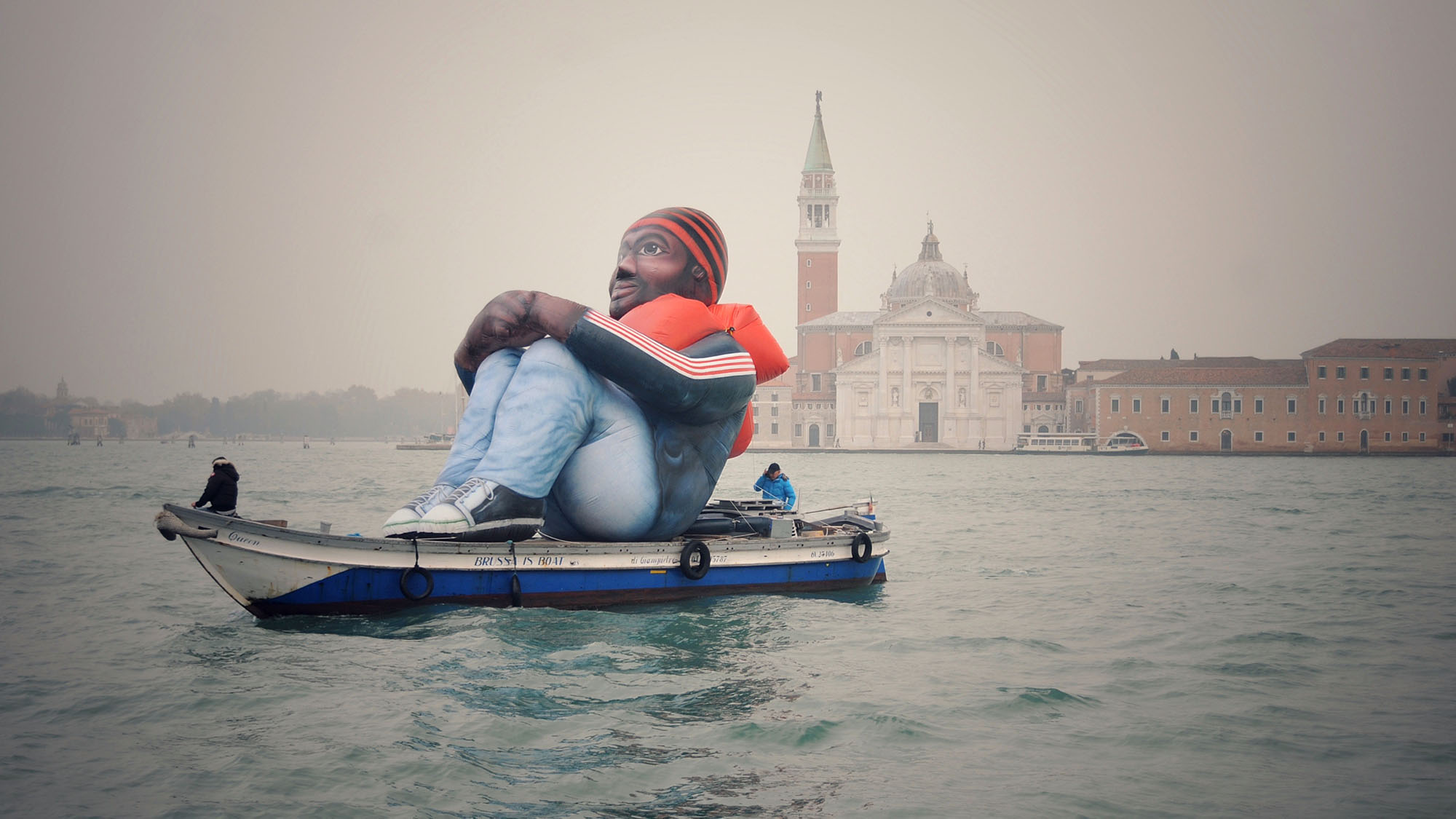 a realistic though clearly inflatable man in a life vest sits atop a boat in venice