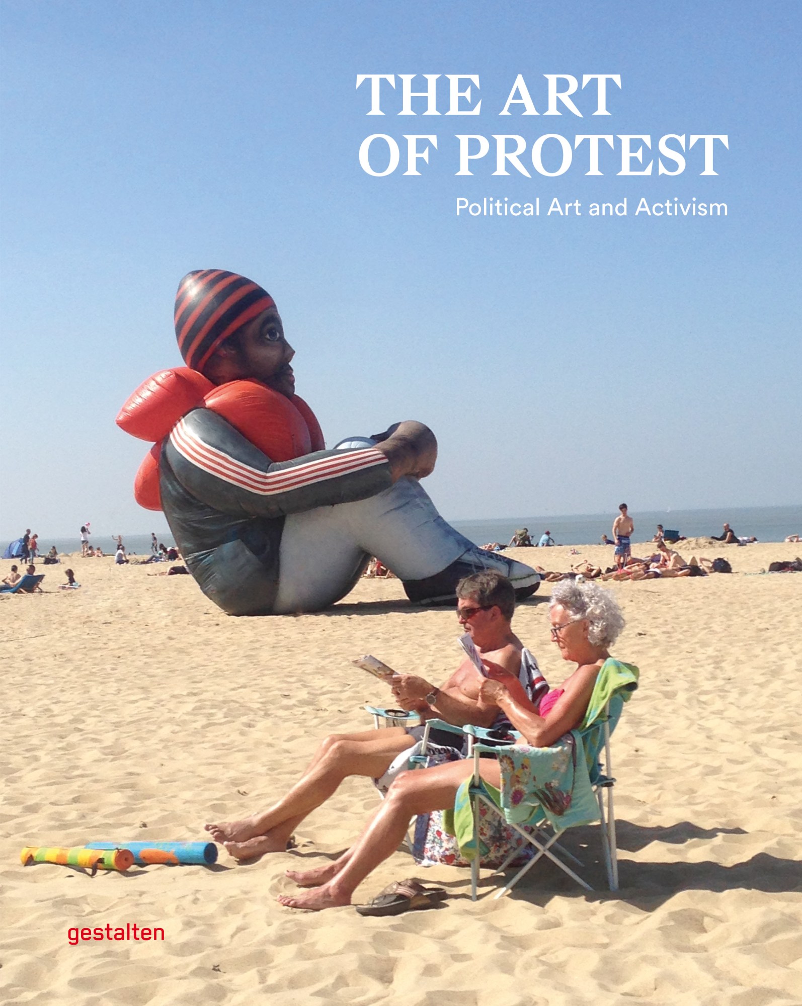 two elderly people read on a beach in front of a realistic though clearly inflatable man in a life vest