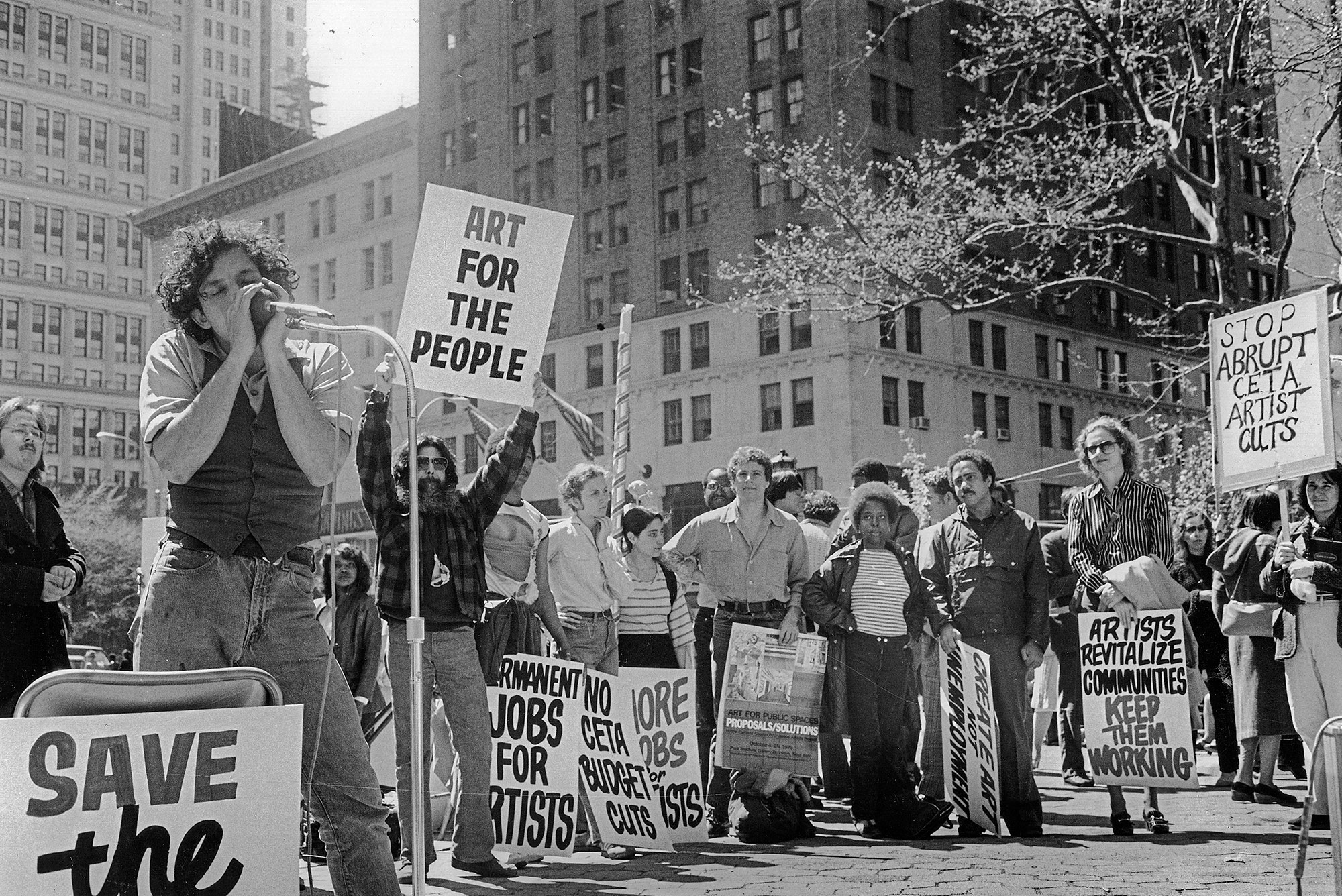 a crowd of people protesting CETA artists cuts in the 1970s, in a built up city area