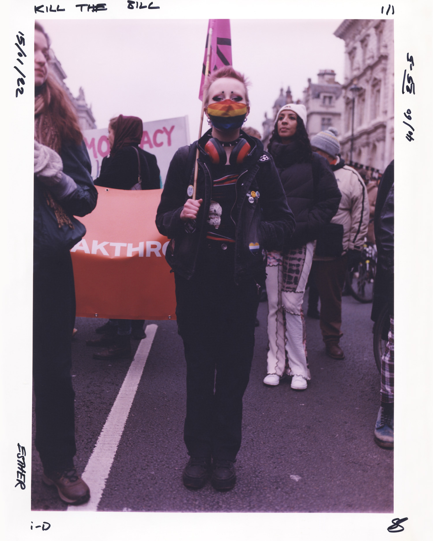 Protesters in all black and a rainbow face mask holding a pink flag at the Kill the Bill protest