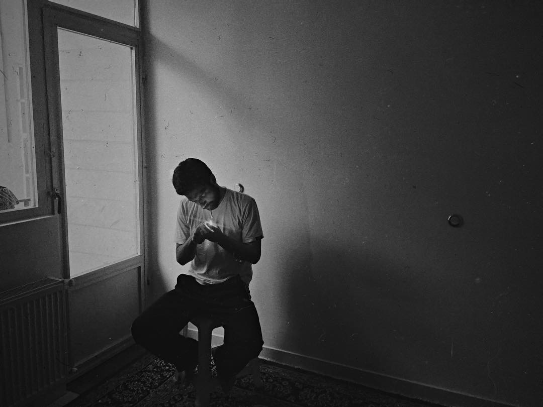 Man sits by a door in an empty room lighting a cigarette