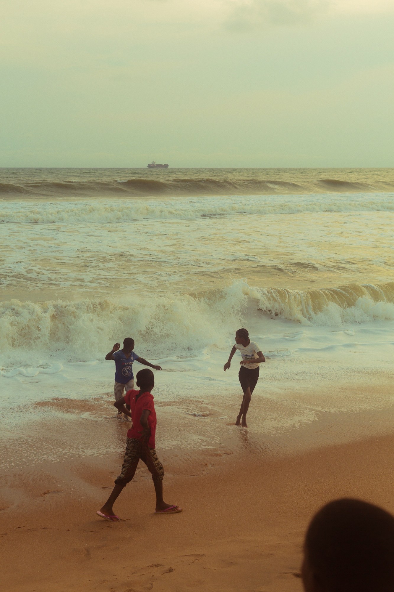 Three boys play on the beach where the tide hits the shore.