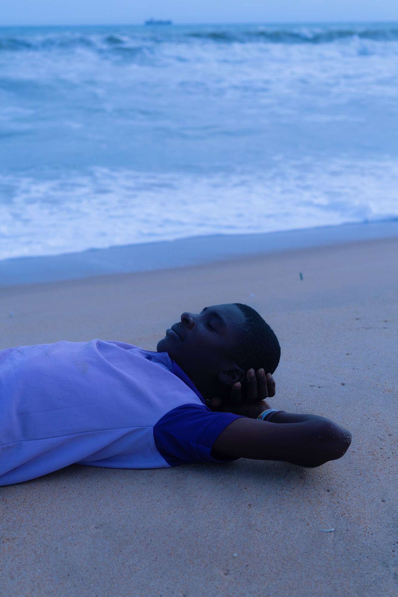 boy sunbathing on the sandy beach next to the incoming tide.