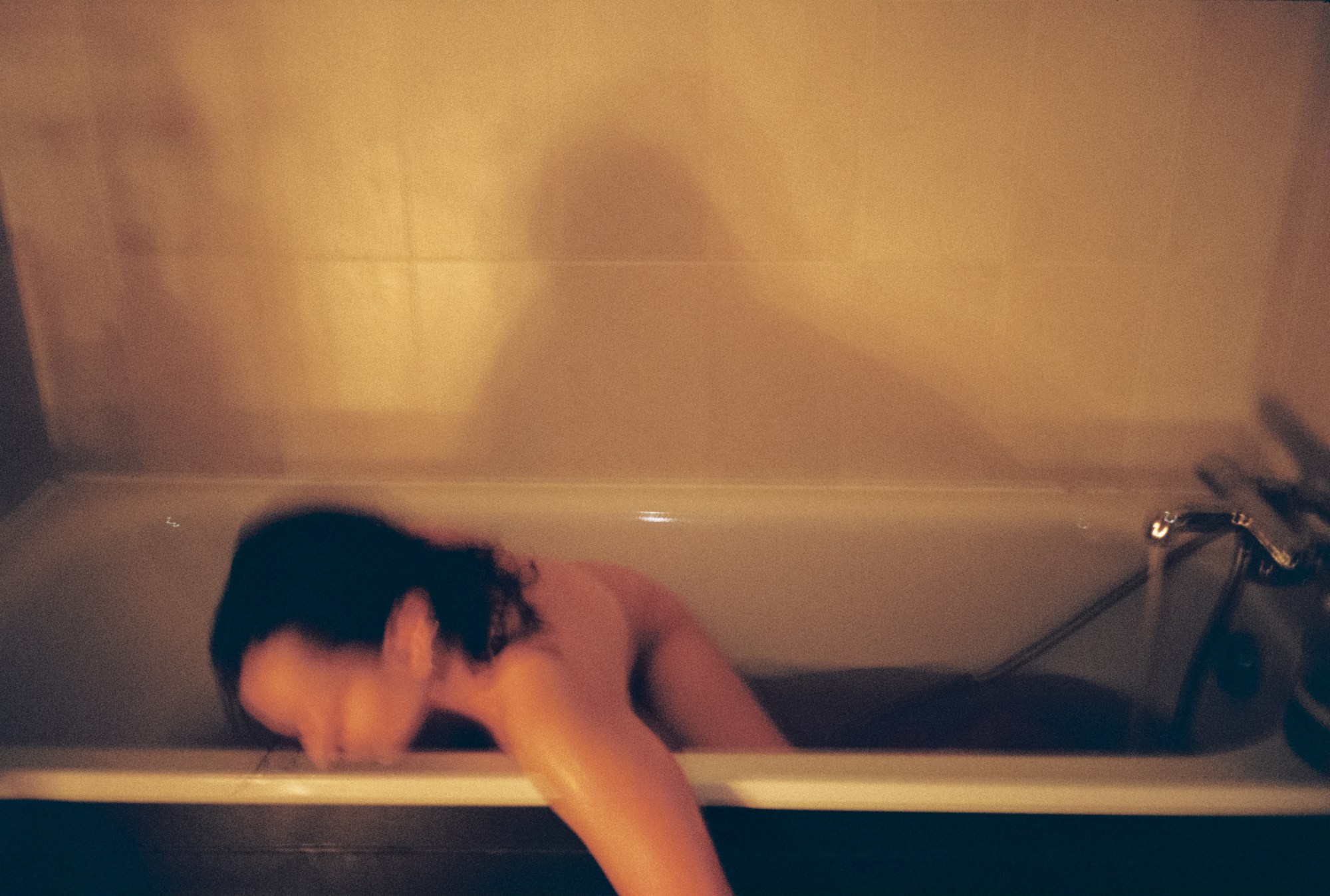 Blurry photo of someone leaning over the edge of a filled bath tub.