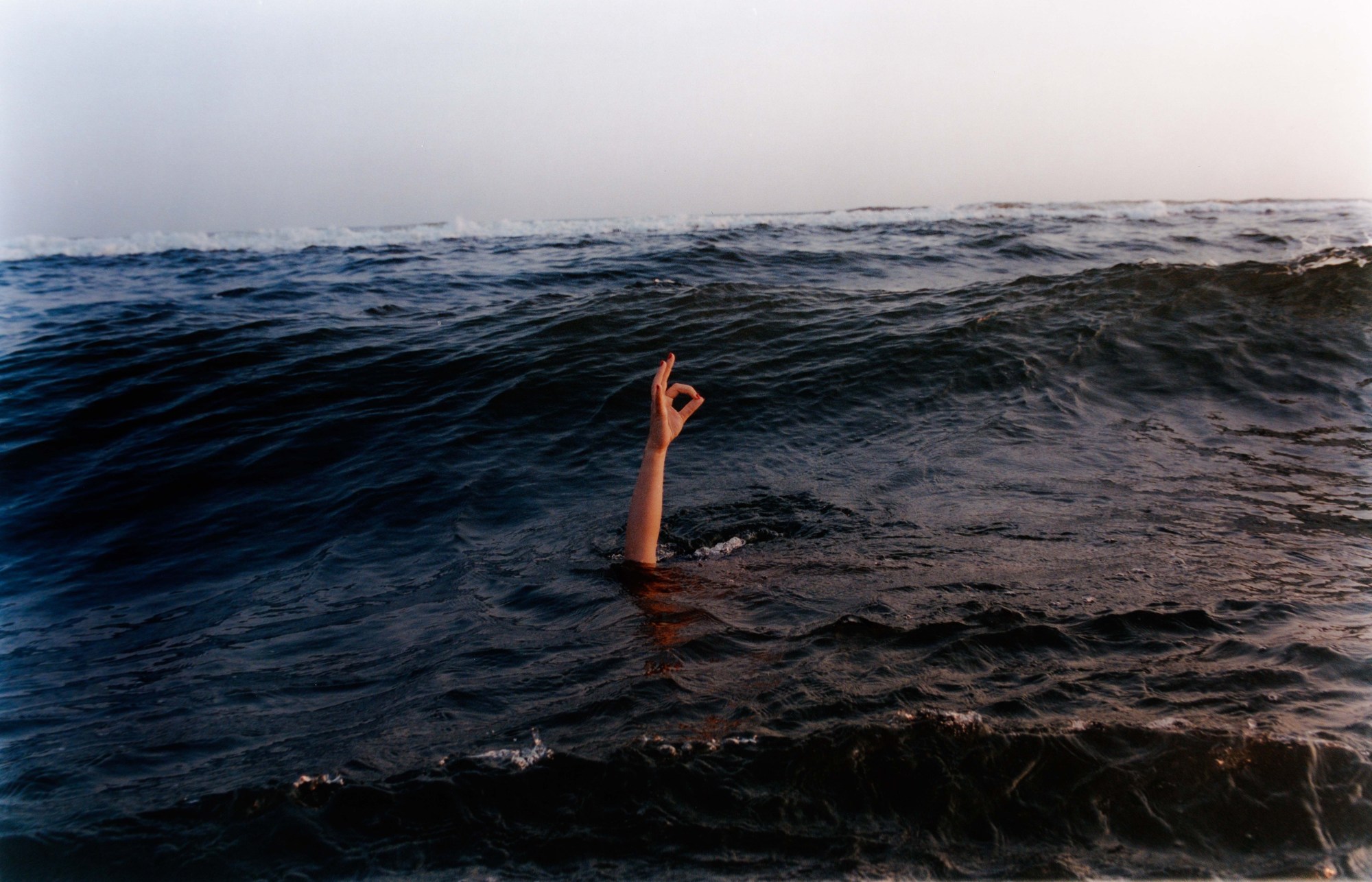 A hand sticking out of the ocean doing an ok sign.