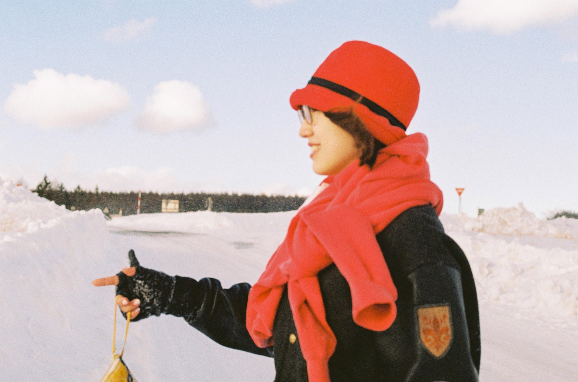 Girl in a coat and scarf and hat in the snow pointing out in front of her.