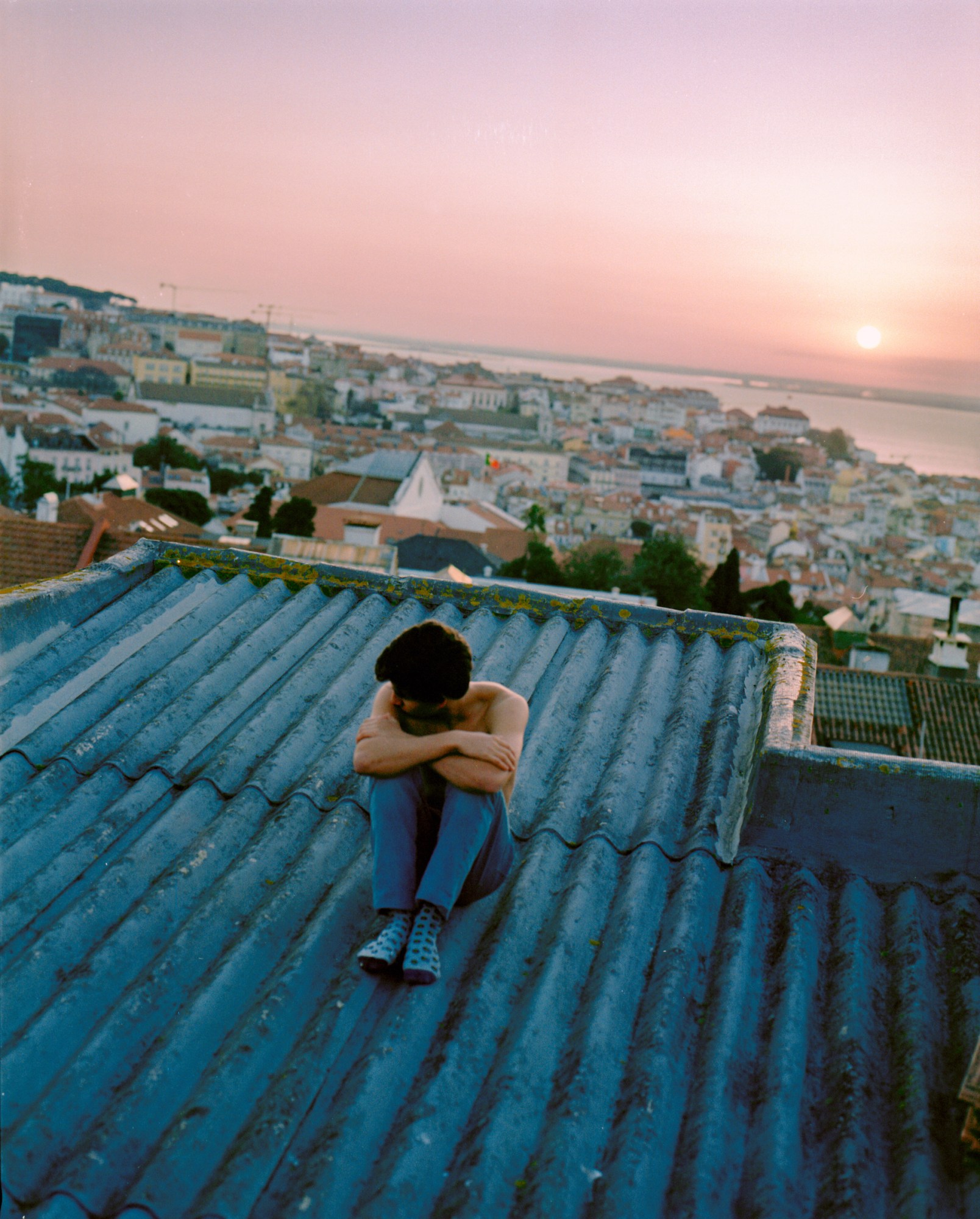 Shirtless man sitting on the roof at sunrise.