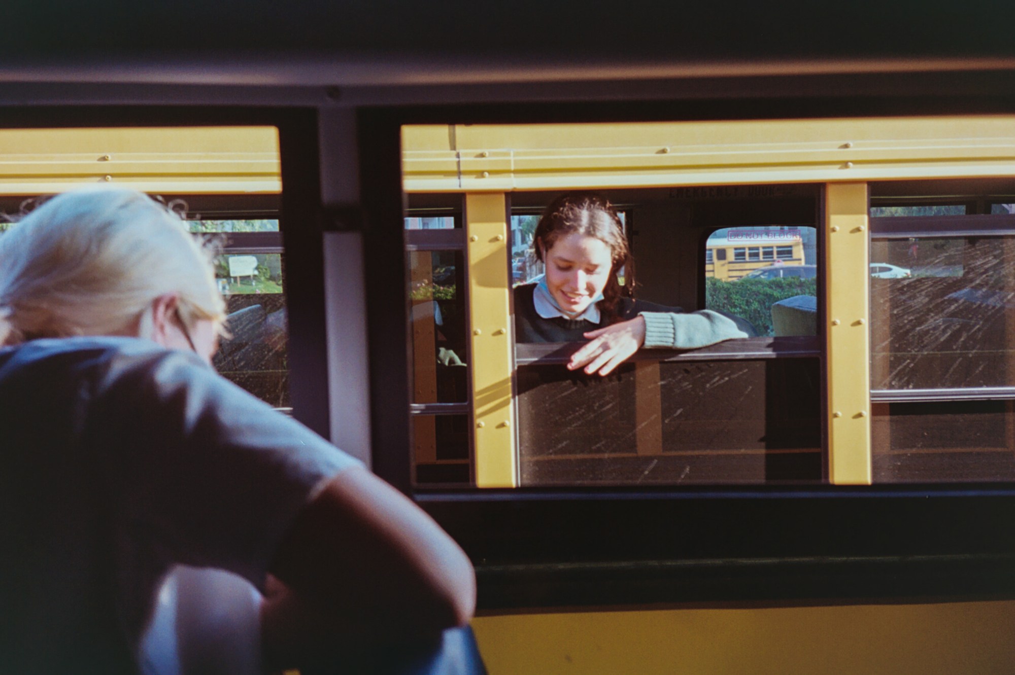 A girl hangs out of a school bus window