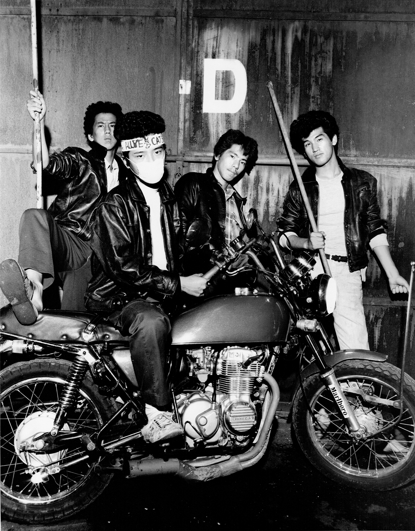 a group of young japanese men wearing leather jackets around a motorcycle in the 70s by seiji kurata