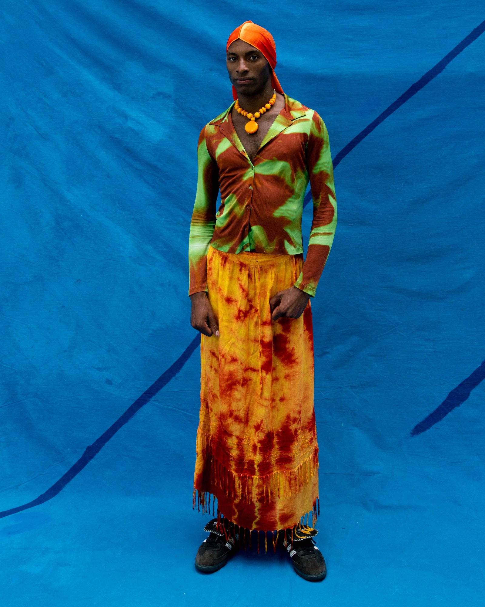 a model wearing colourful clothes stands in front of a blue painted backdrop