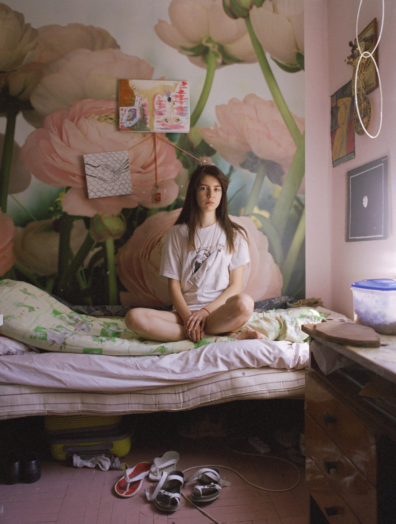 model sits cross legged on a single bed in a pastel pink room