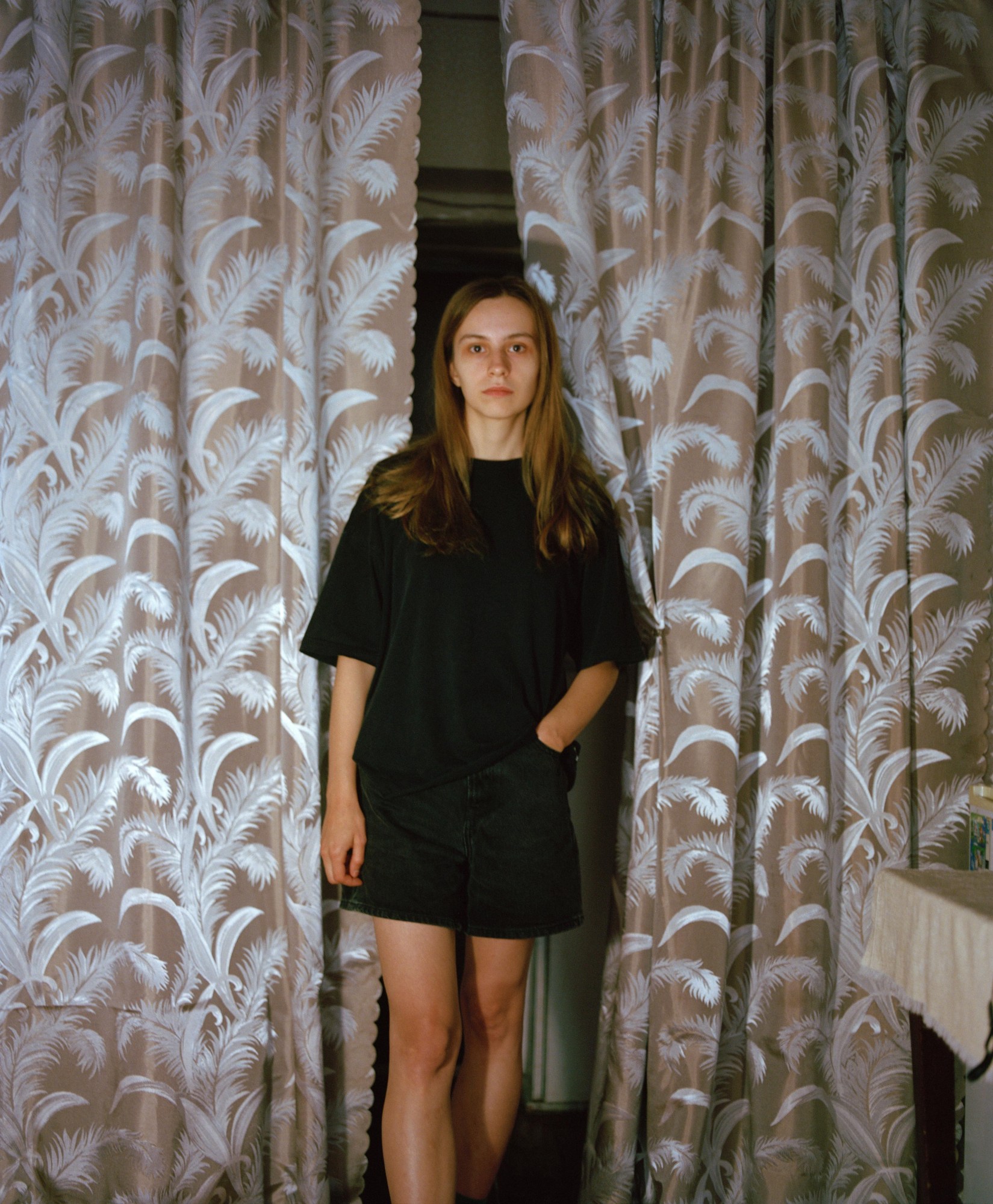 model wearing just a large dark t-shirt stands between a set of feather-pattern curtains