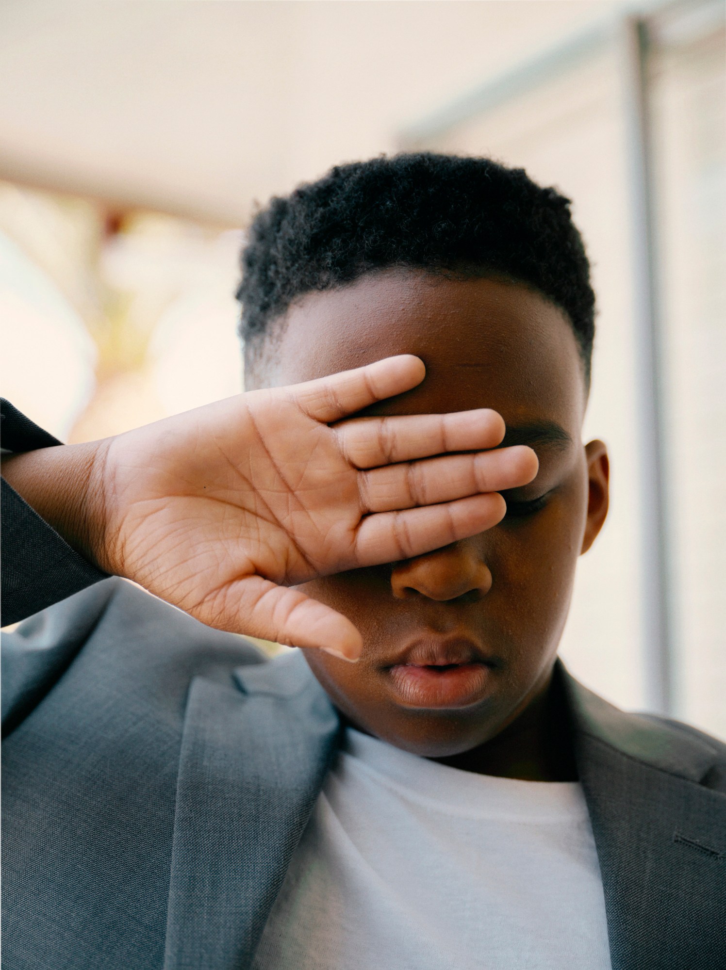 a young boy holds a hand out across his face