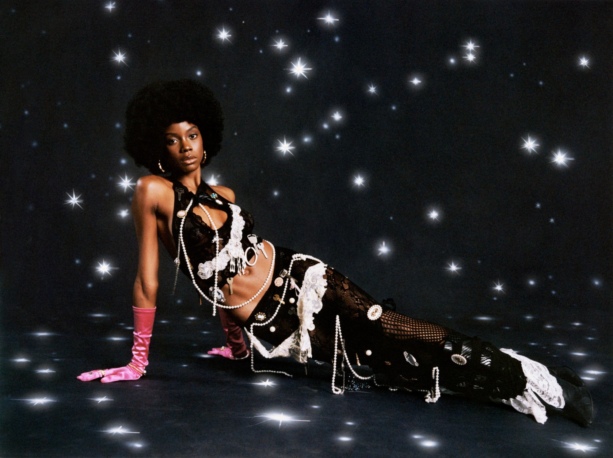 a woman poses on the floor of a black studio full of stars