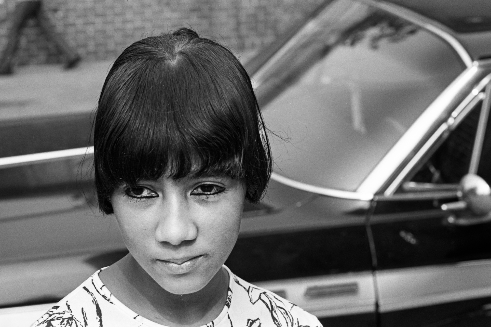 black and white photo close up of teenage girl in front of car