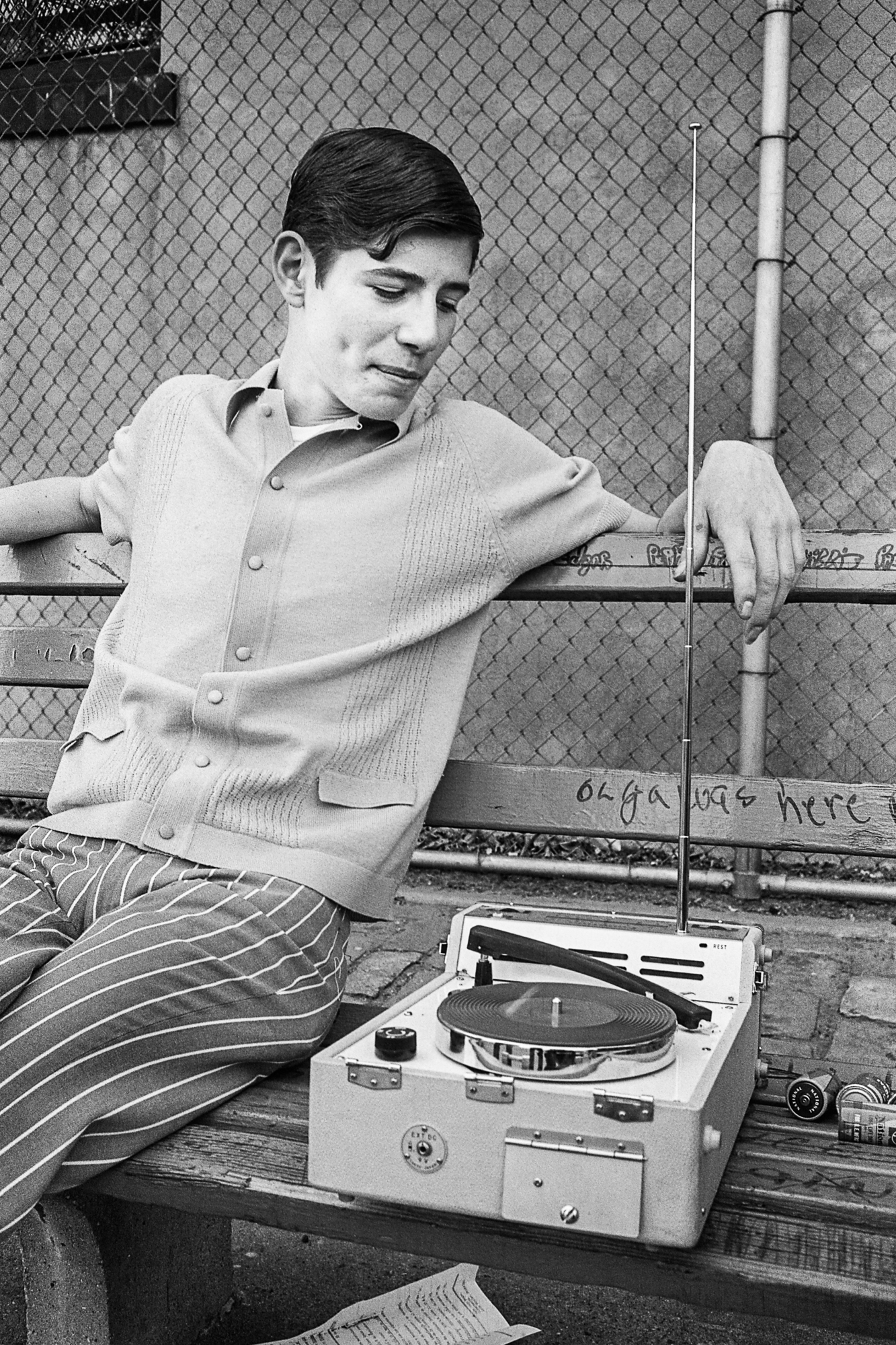 black and white photo of teenage boy listening to record player on park bench