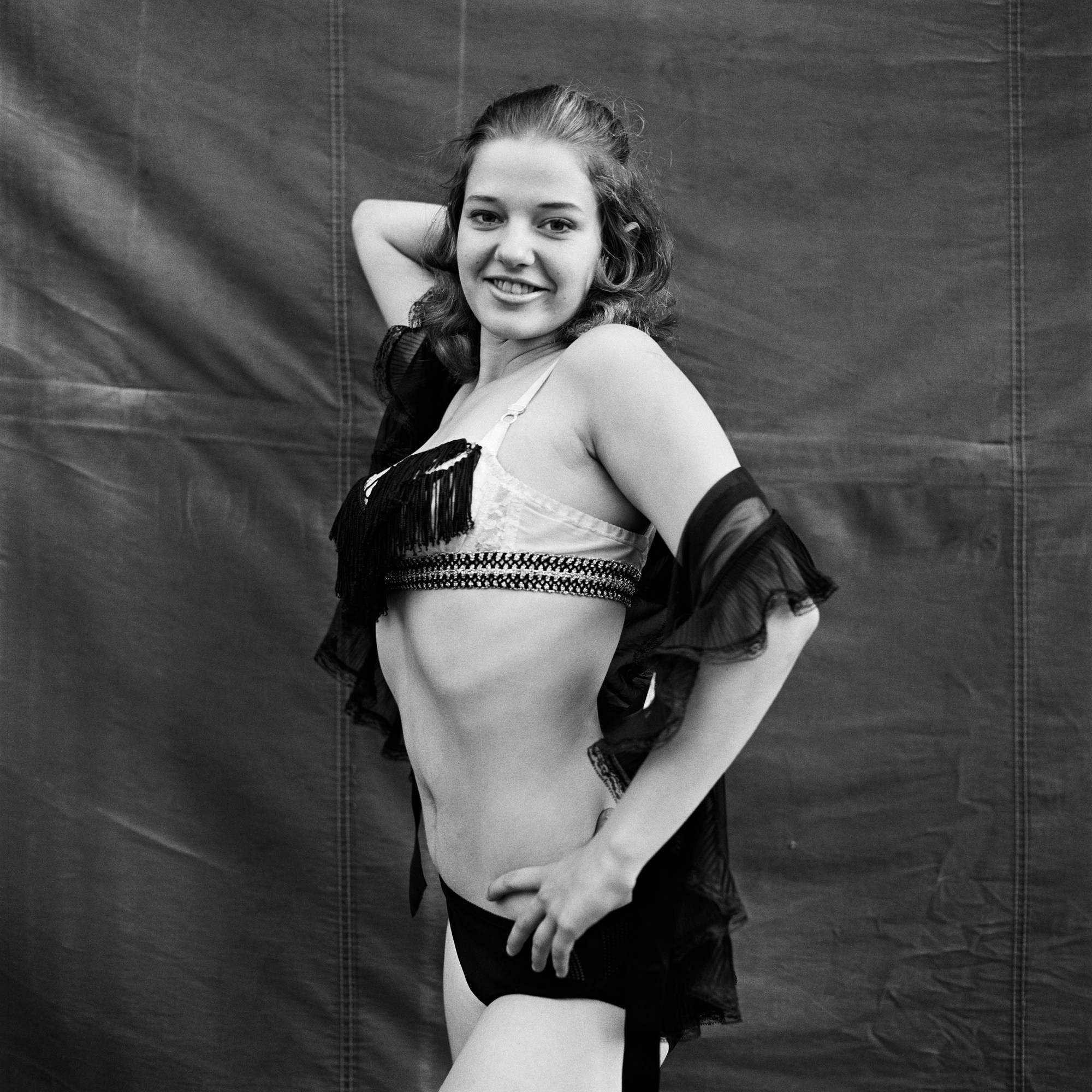 A woman in fringe covered lingerie poses in front of a tent.