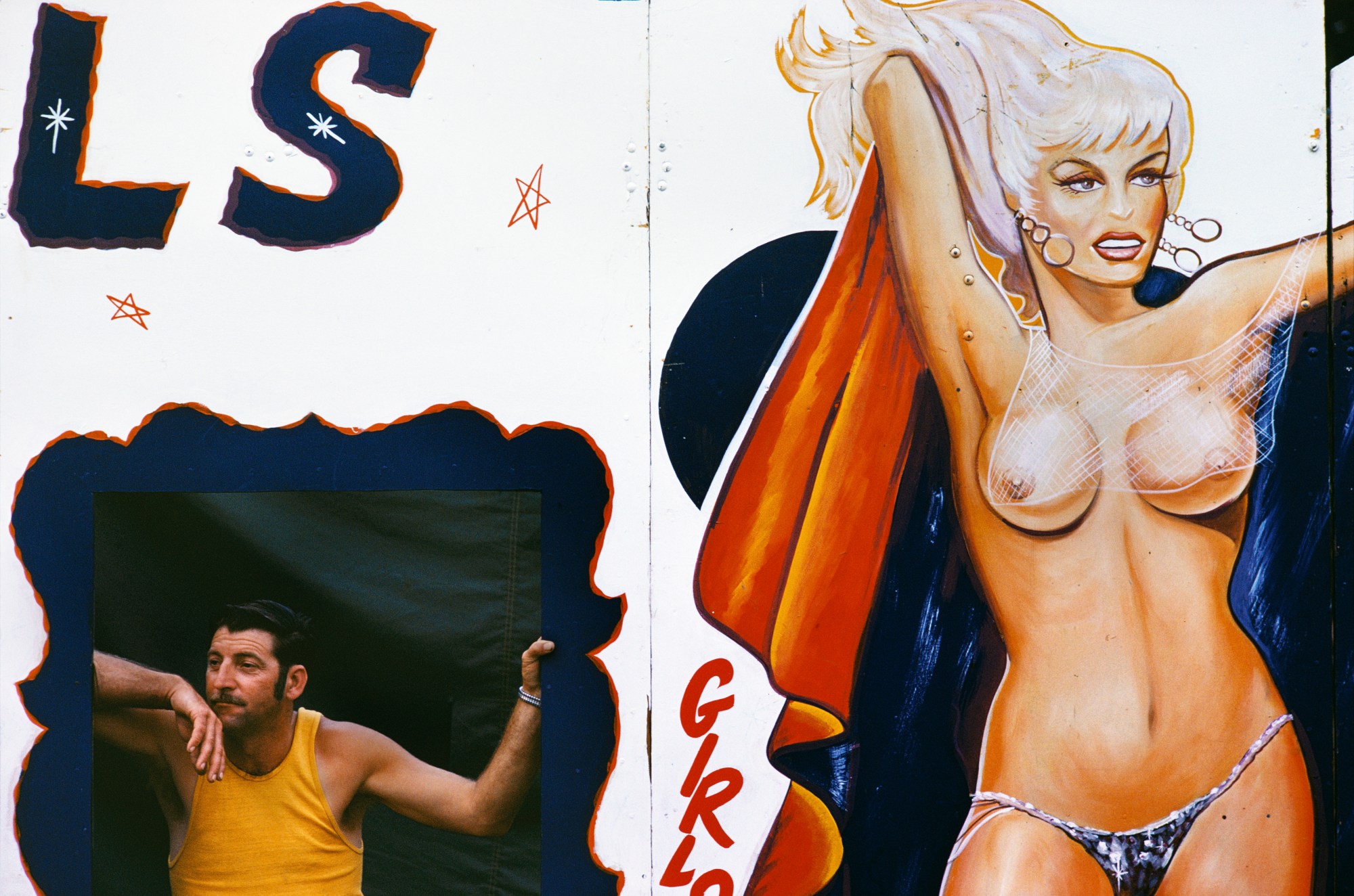 A man stands in the cut out of a wall with a naked woman painted on it.