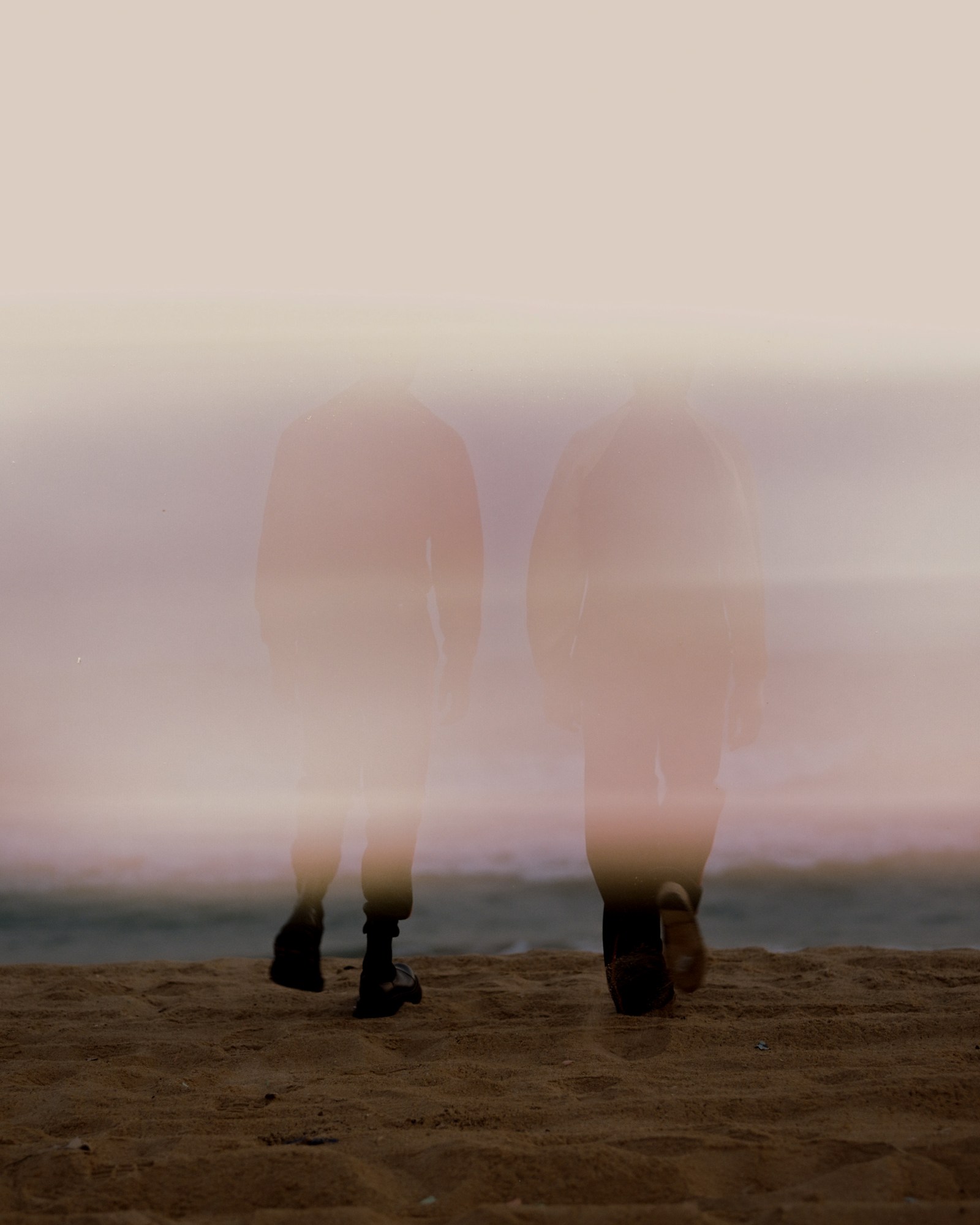 two models walk towards the sea on a sandy beach in silhouette and obscured by light