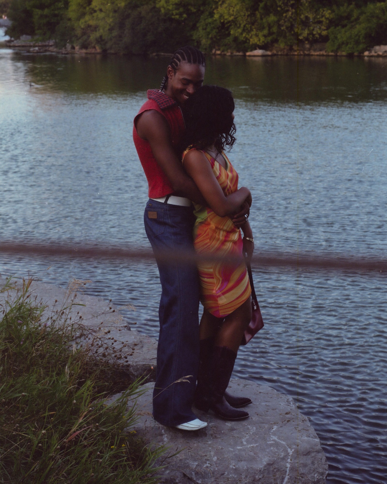 a couple stand in embrace by a body of water at sunset