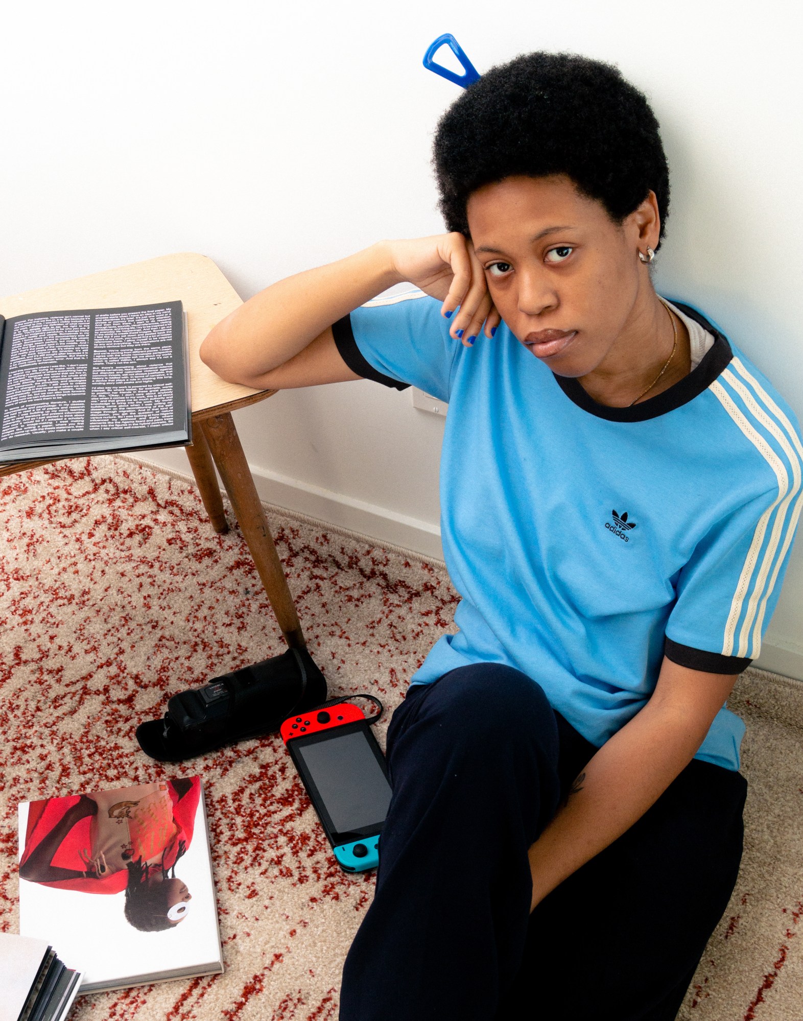 a woman in a blue t-shirt sits on the floor and rests her arm on a table