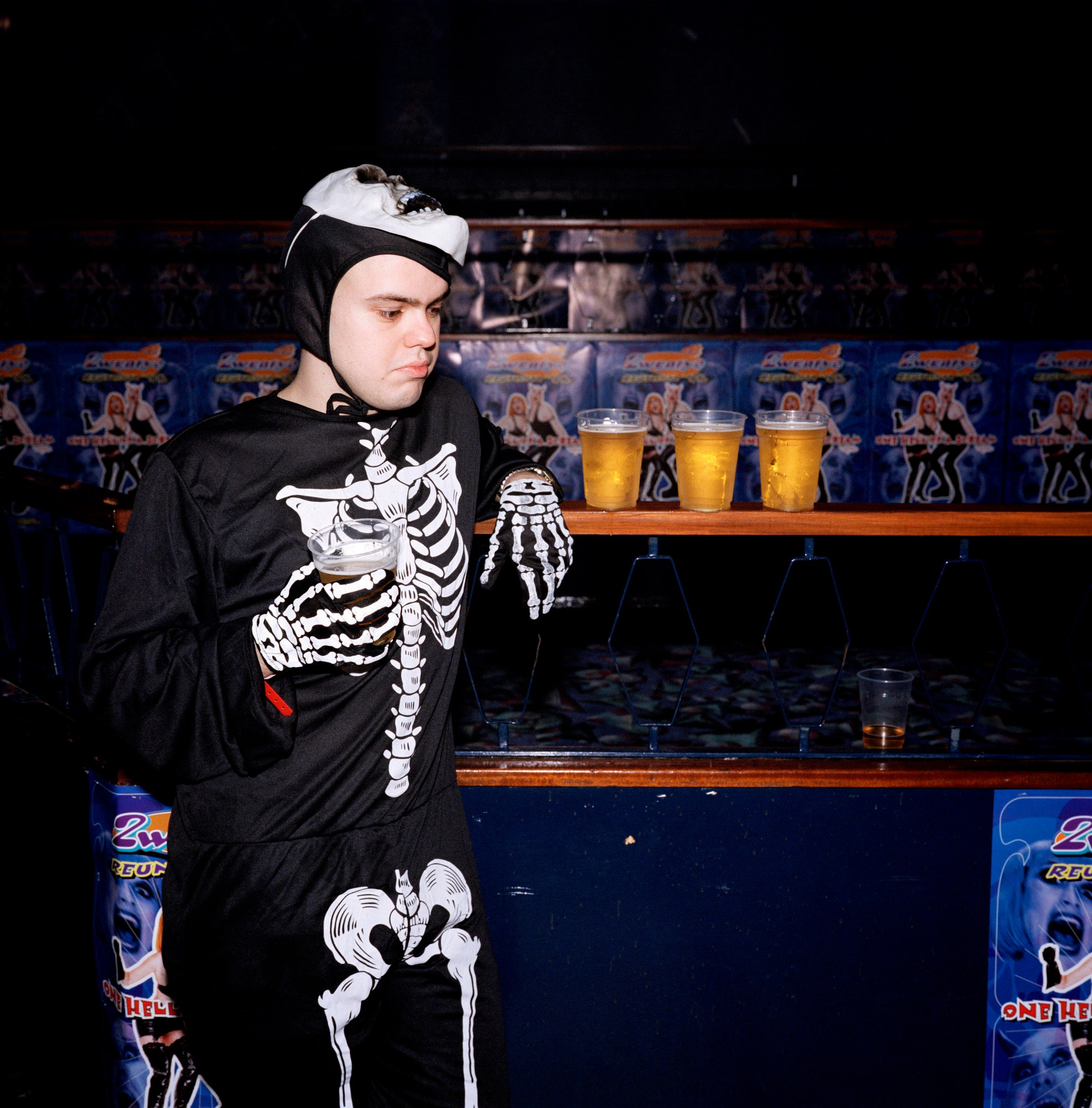 Man in skeleton onesie drinks a pint from plastic glass in a nightclub