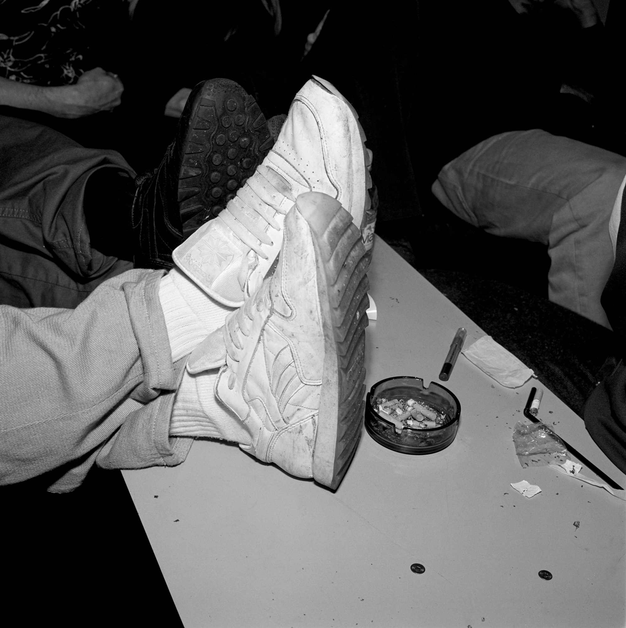 Black and white close up of white trainers on table next to ashtray