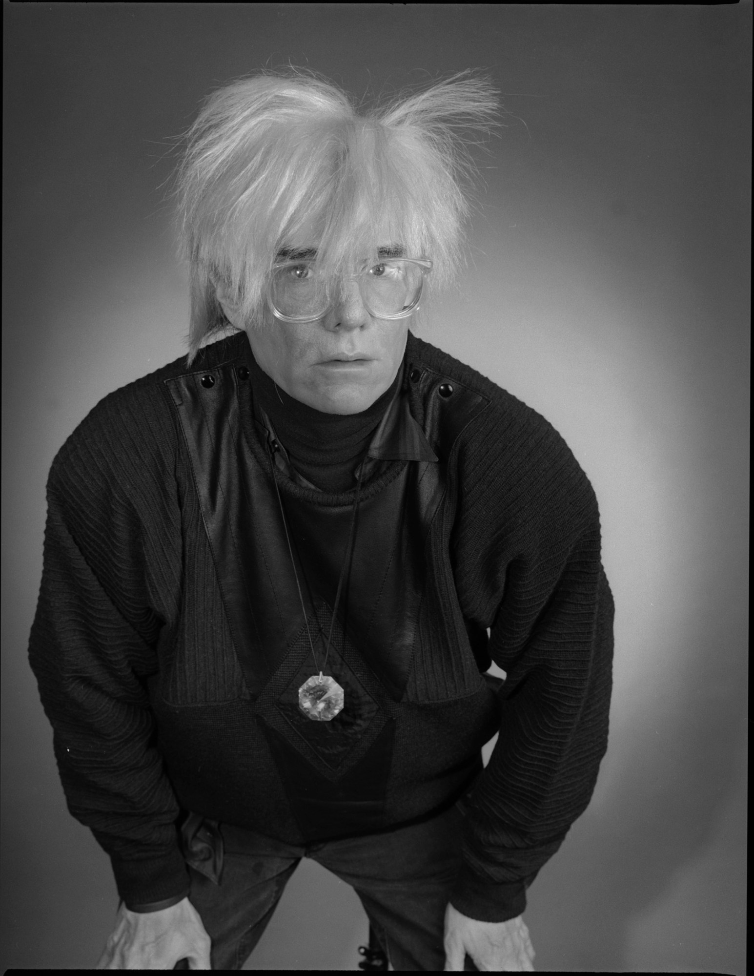 andy warhol with his hands on his knees in a black and white image by christopher makos