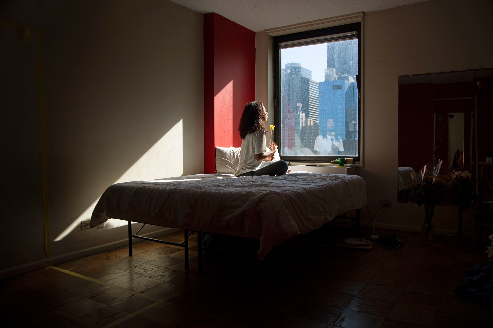 a self-portrait of kia labeija holding a yellow flower and looking out the window of a new york hospital