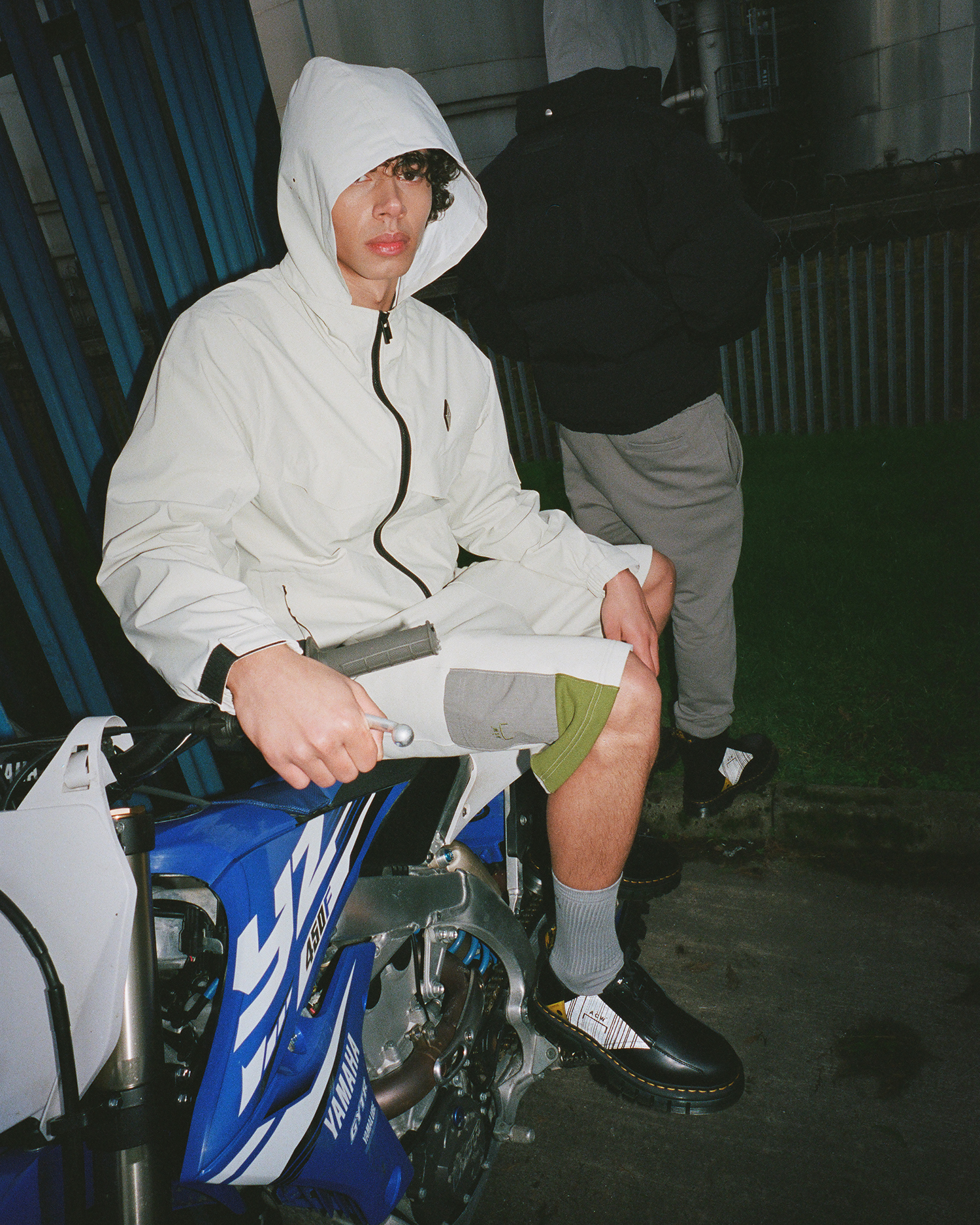 a man sitting on a yamaha motorbike wearing dr martens by a cold wall