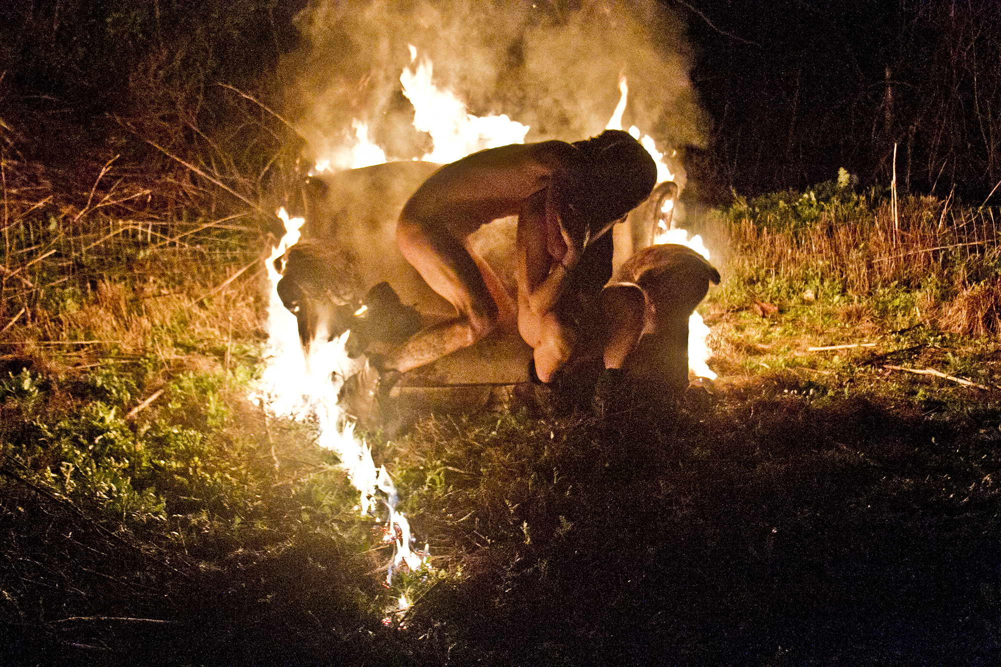 two naked people make out on a sofa surrounded by fire