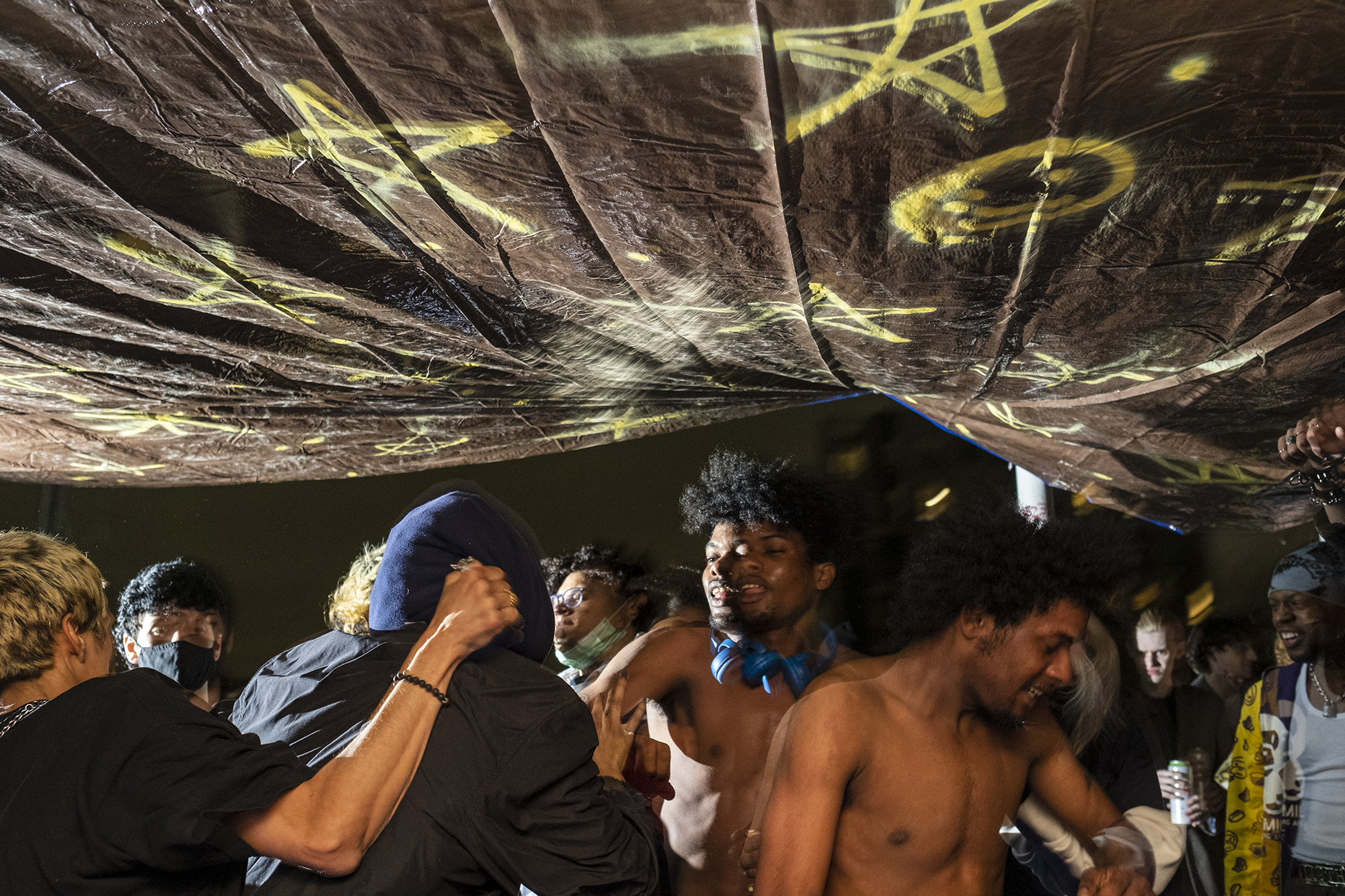 a group of black and latino ravers dance in a DIY tent under strobe lighting