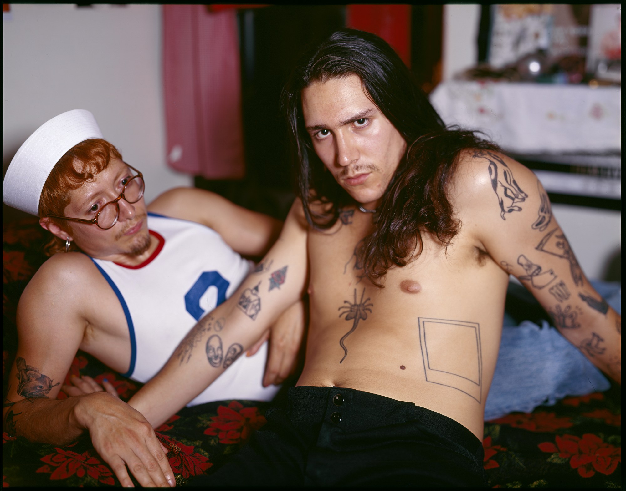 a portrait of a queer couple with tattoos lying on a bed by ian lewandowski