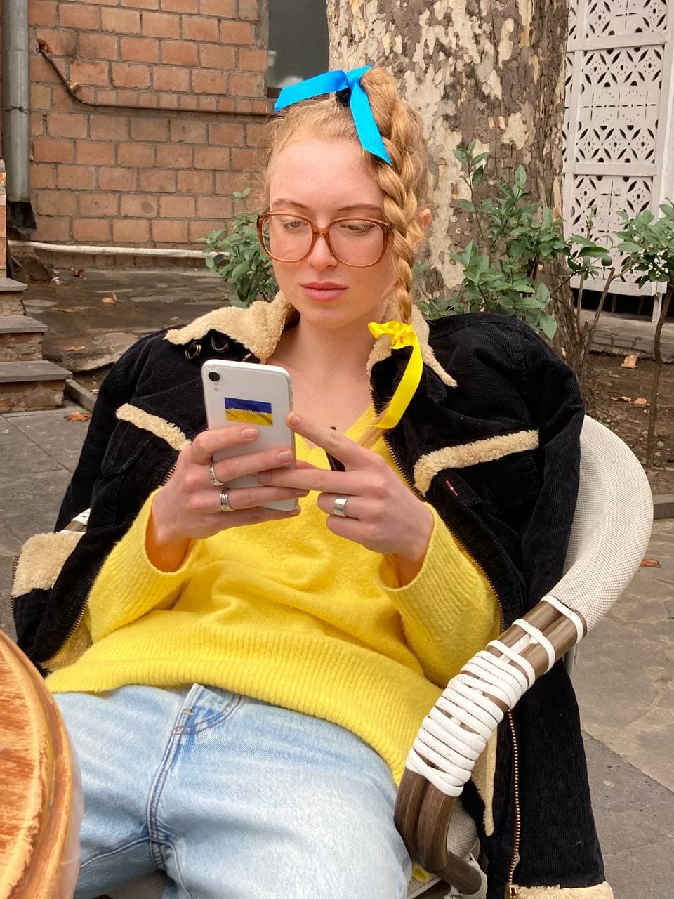 a woman in a yellow jumper and large glasses reclines in a chair