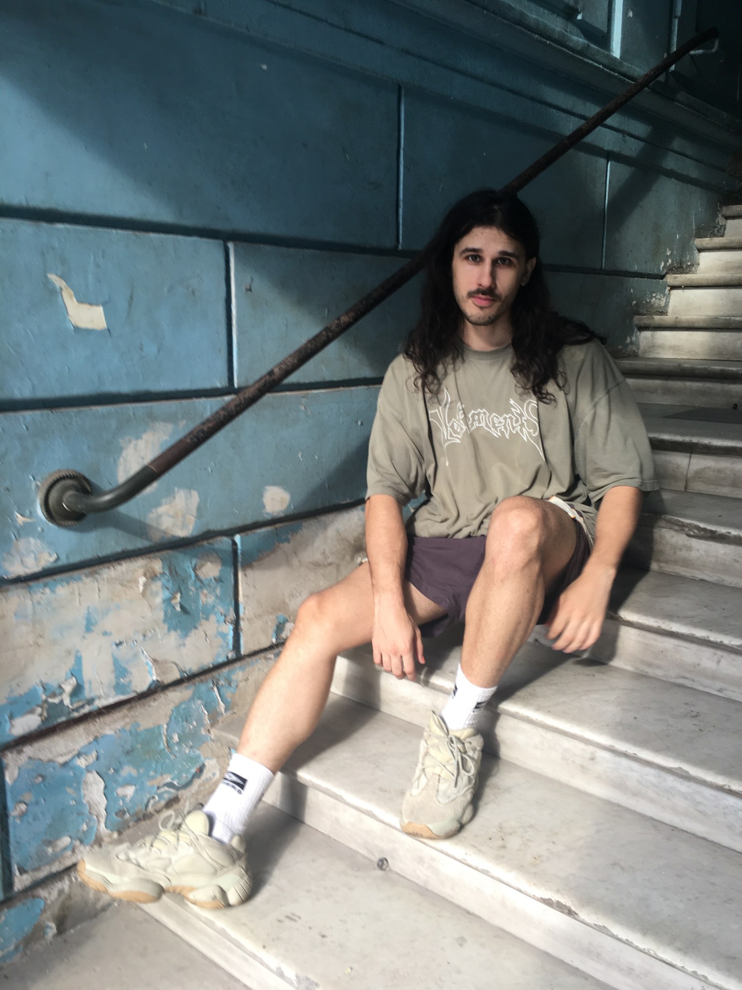 a man wearing shorts and a vetements tee sits in a staircase