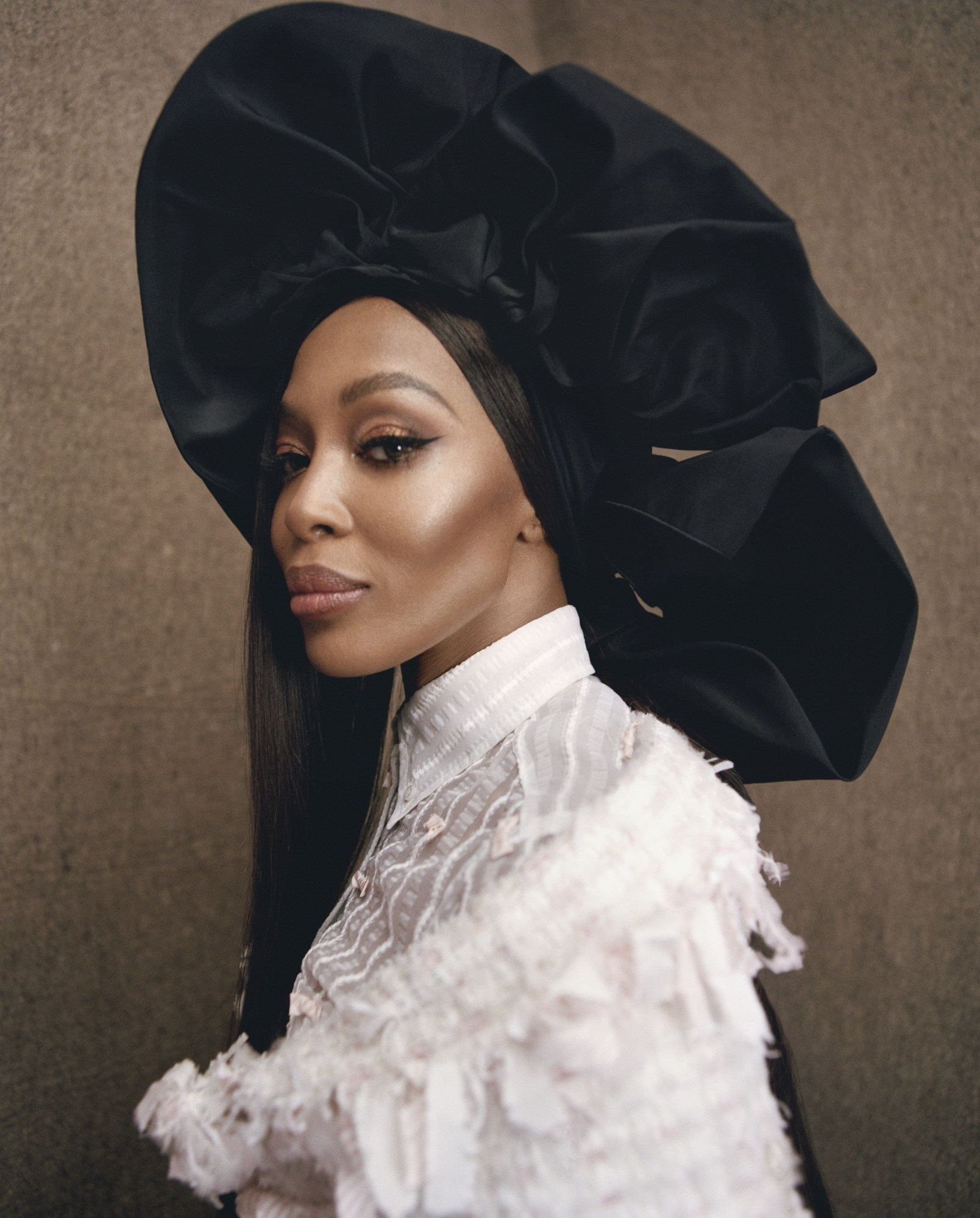 Naomi Campbell wearing a black hat and white blouse.