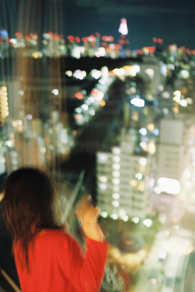 Girl pressed against the window overlooking the city skyline.