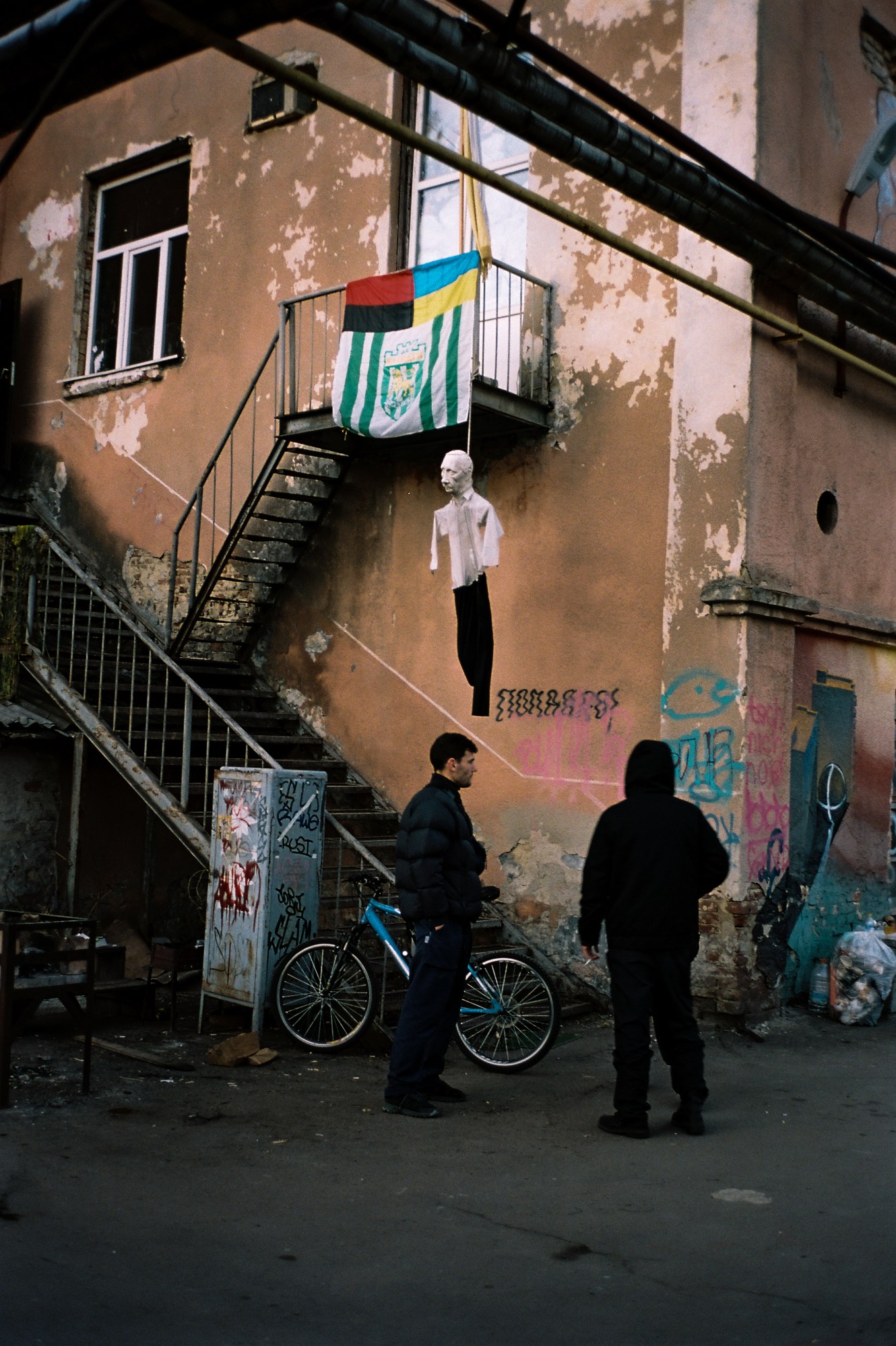 Two men standing outside a building with a hung Putin figure from the balcony