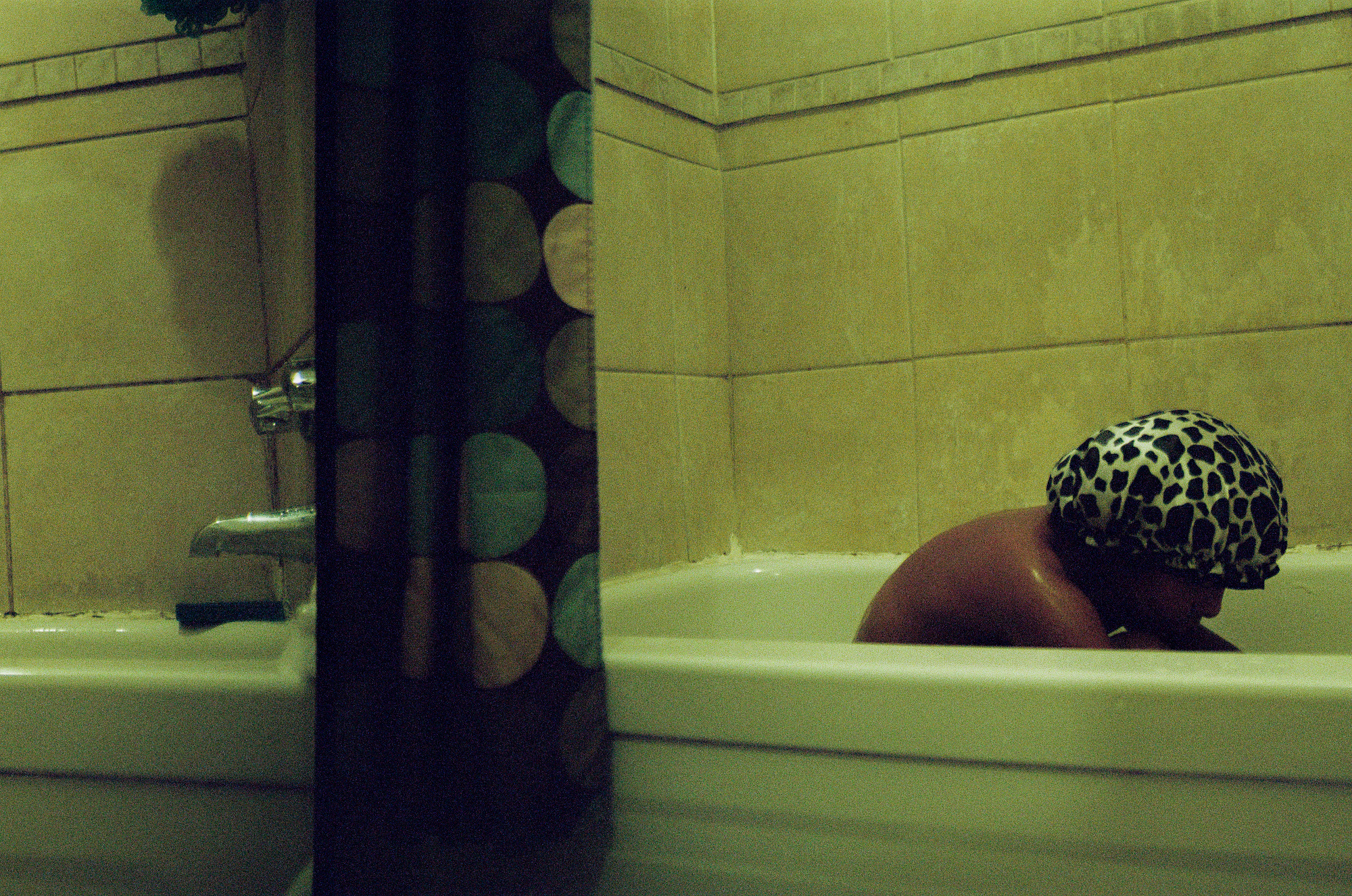 young kid sitting forlorn in the bath with a shower cap on.