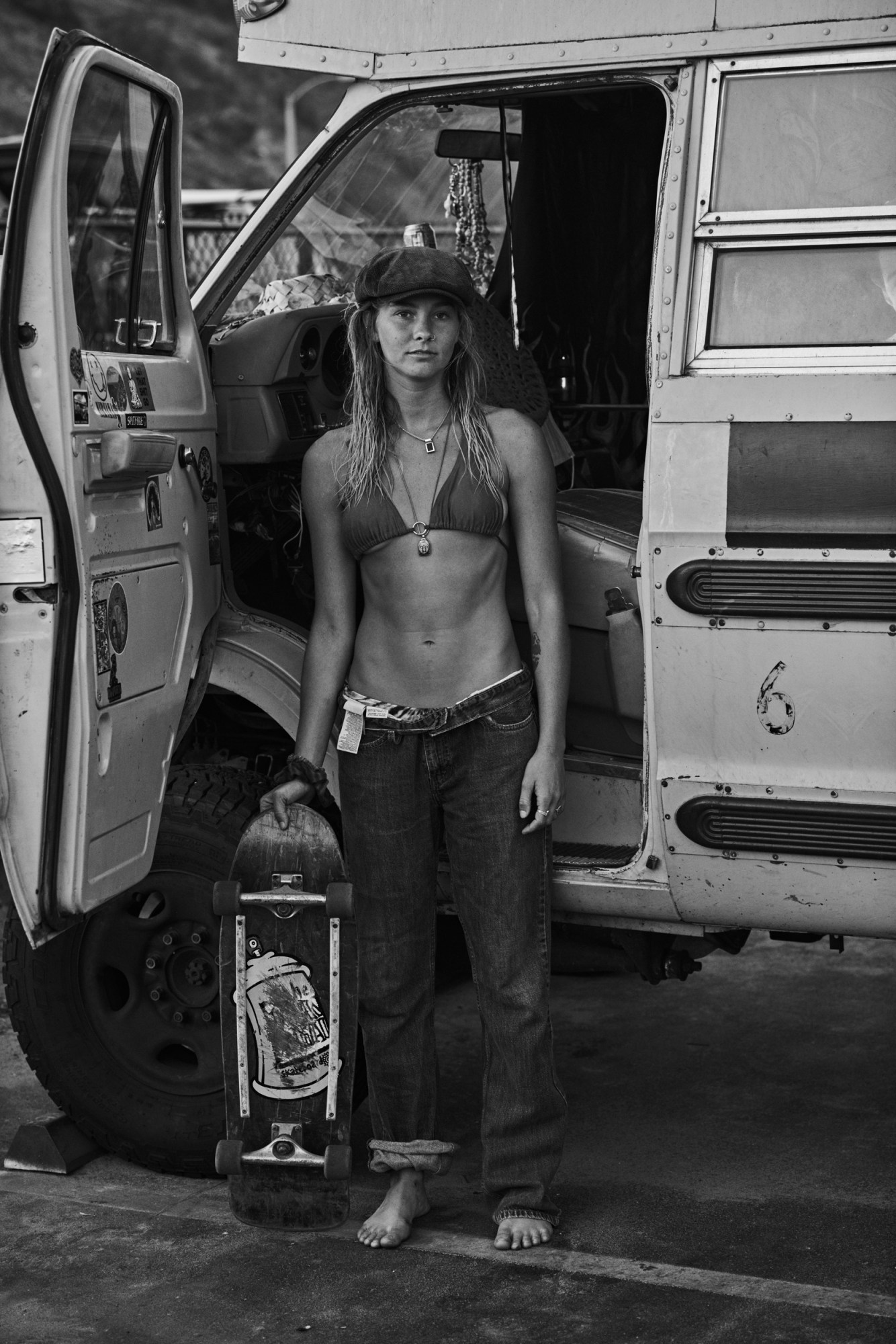 A woman wearing a bikini and jeans holding a skateboard.