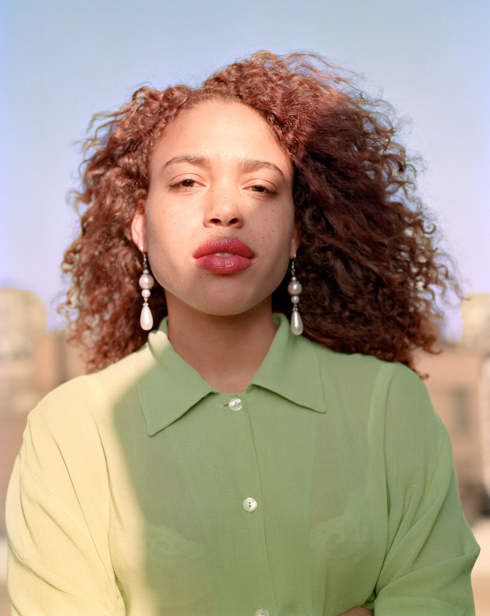 portrait of a redheaded model in a green shirt and long pearl earrings