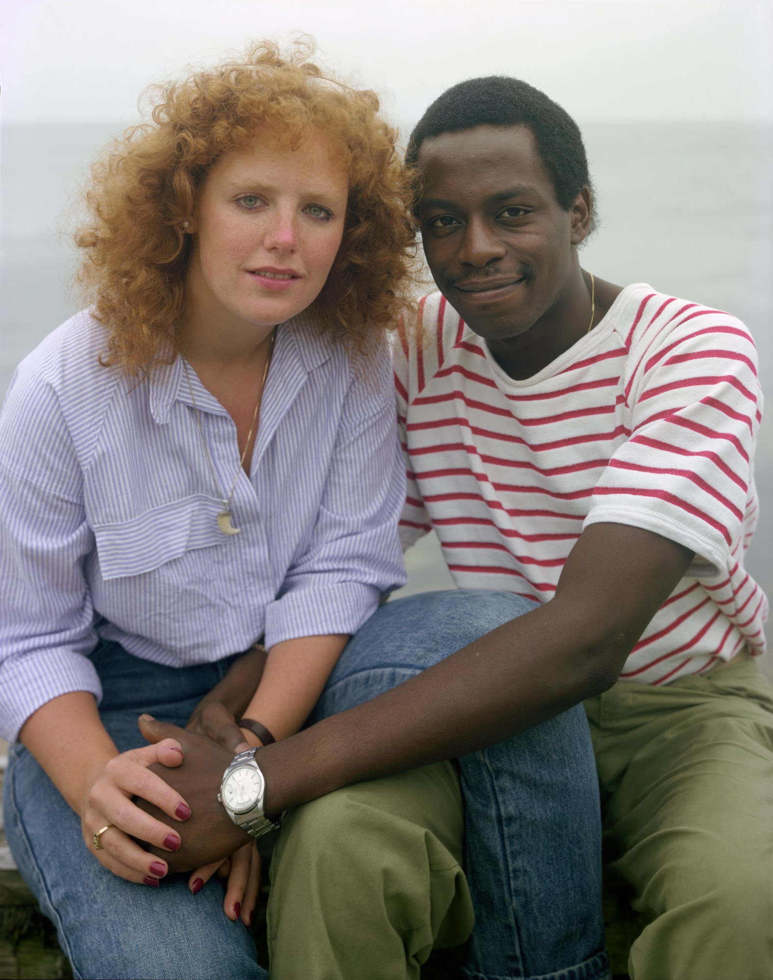 two models sit in close embrace, holding hands with their legs overlapping