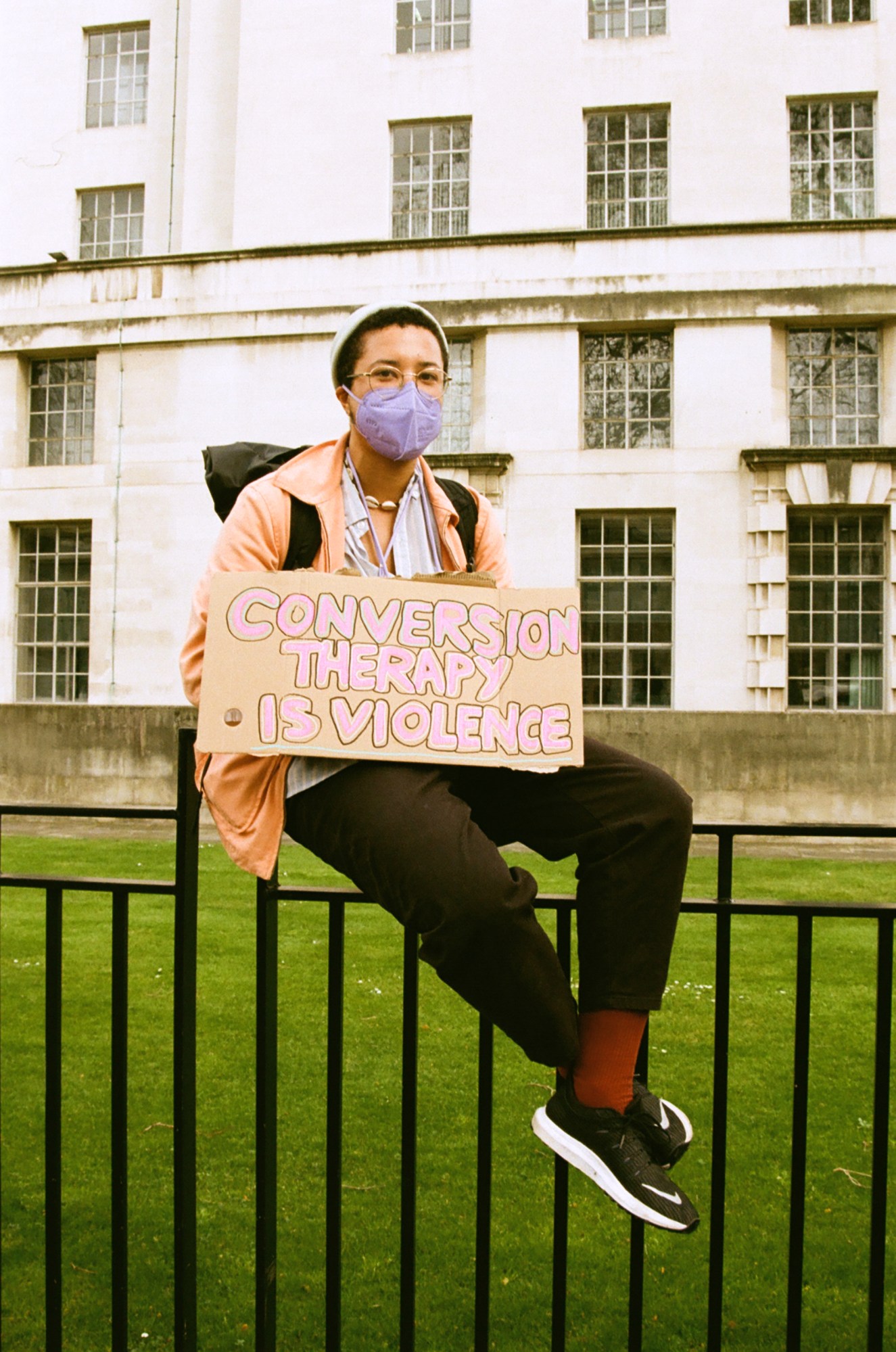 Protester sitting on the fence with a sign saying 'conversion therapy is violence' at the ban trans conversion therapy protest at Downing Street, London.