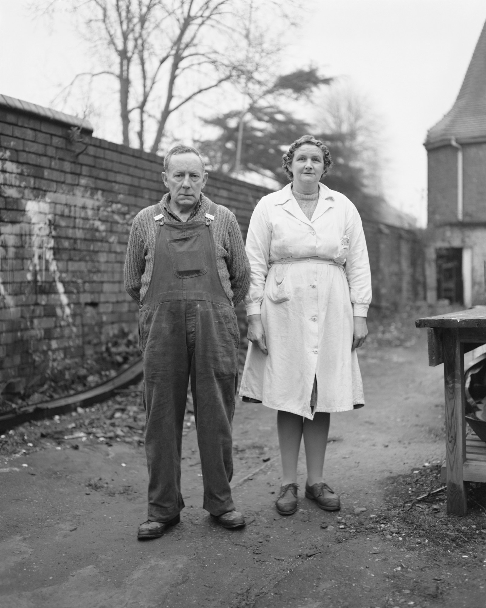 an old man and woman stood by a brick wall