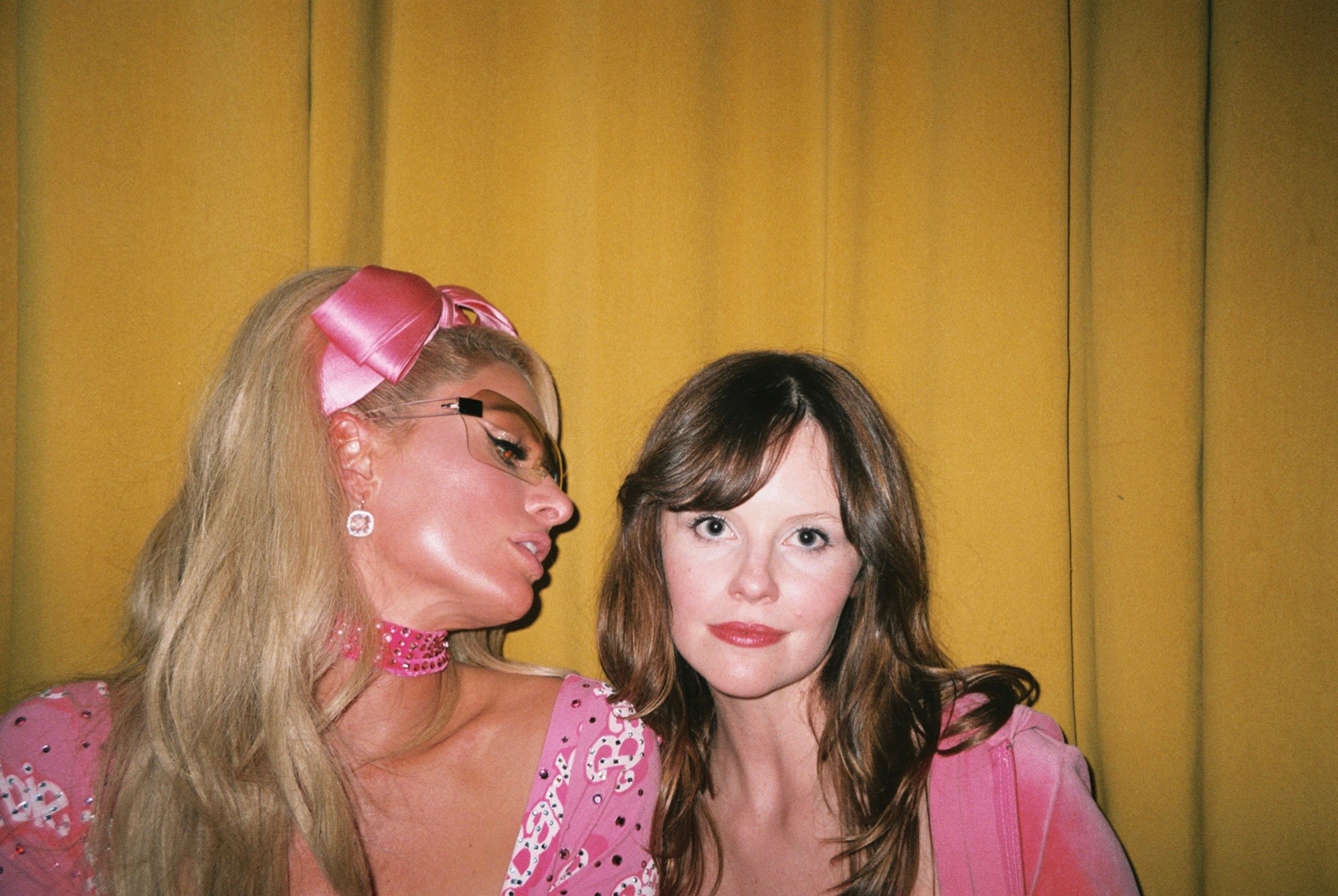 paris hilton and sarah ramos, both wearing pink, pose together in front of a yellow backdrop