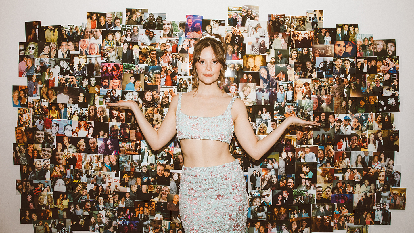 sarah ramos poses in front of a wall of photos